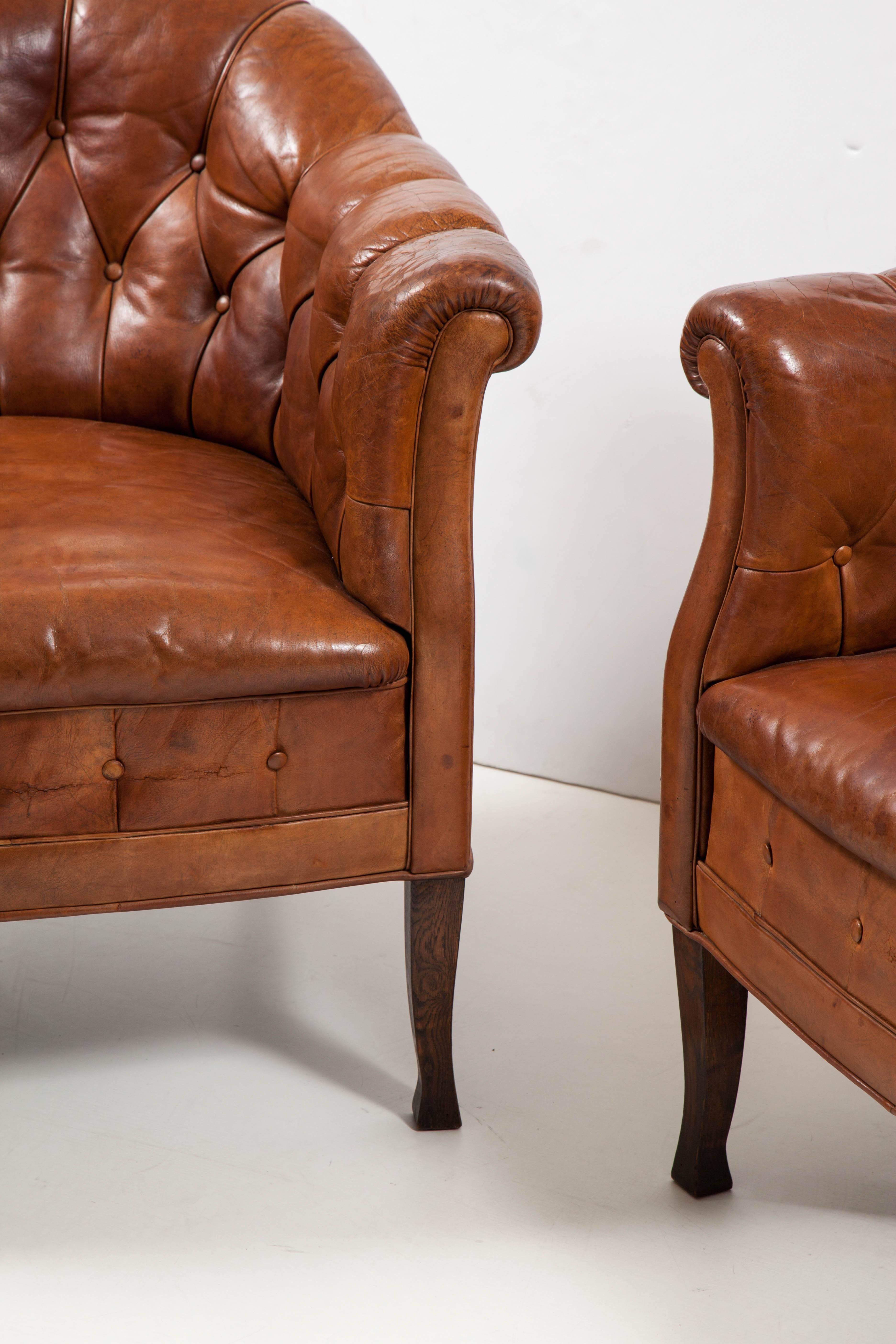 A pair of Swedish tufted leather club chairs, circa 1910-20, of tub back form with scrolled armrest raised on stained beech legs.
Fantastic patina, sit very comfortably. Leather is supple not dry but has old cracks. A few minor repaired holes but