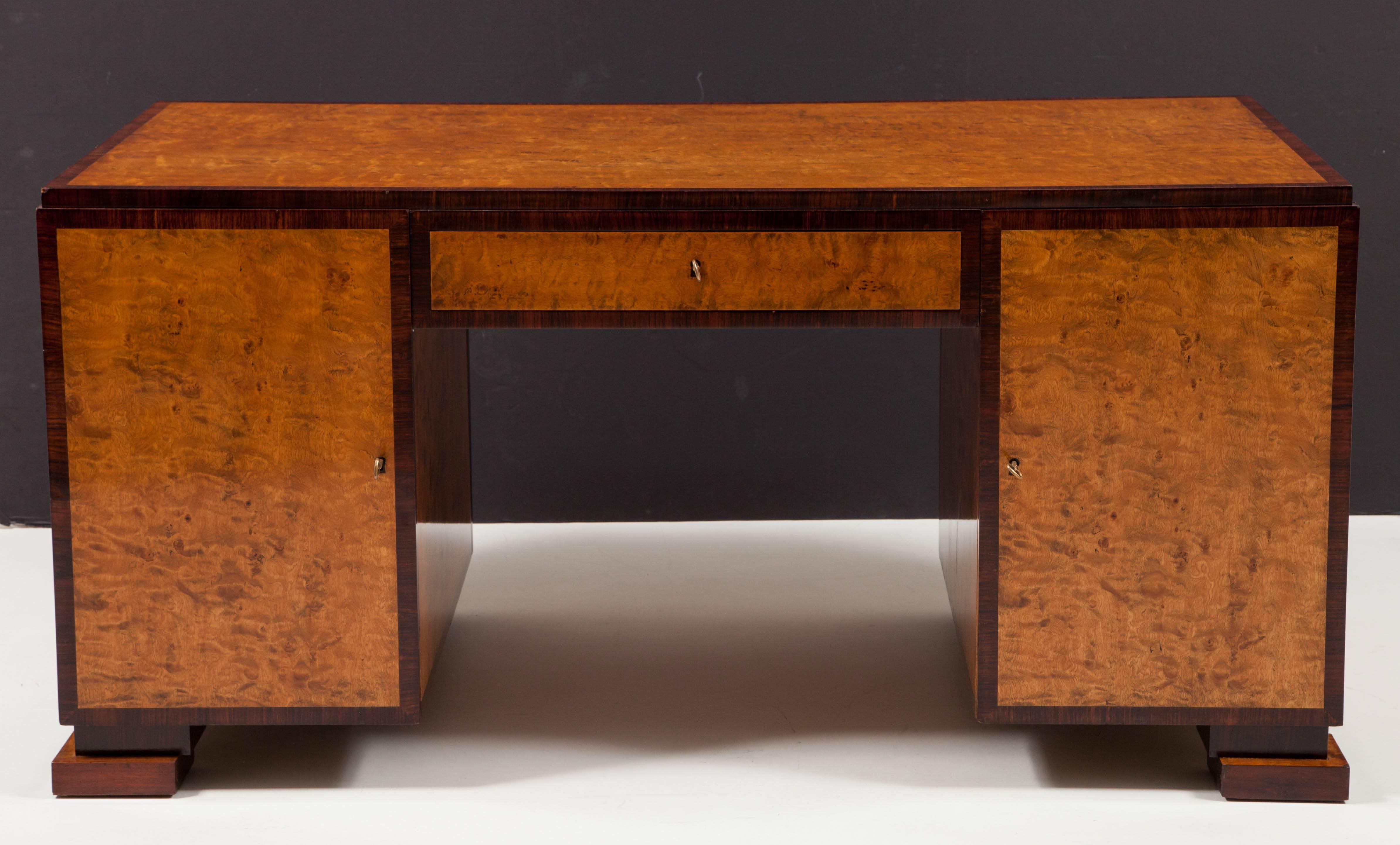 A Swedish Grace figured birchwood and Palisander crossbanded pedestal partners desk, circa 1930-1940, the rectangular stepped top above a central drawer and two pedestal cabinets with cupboard doors, enclosing drawers and shelves, raised on floating