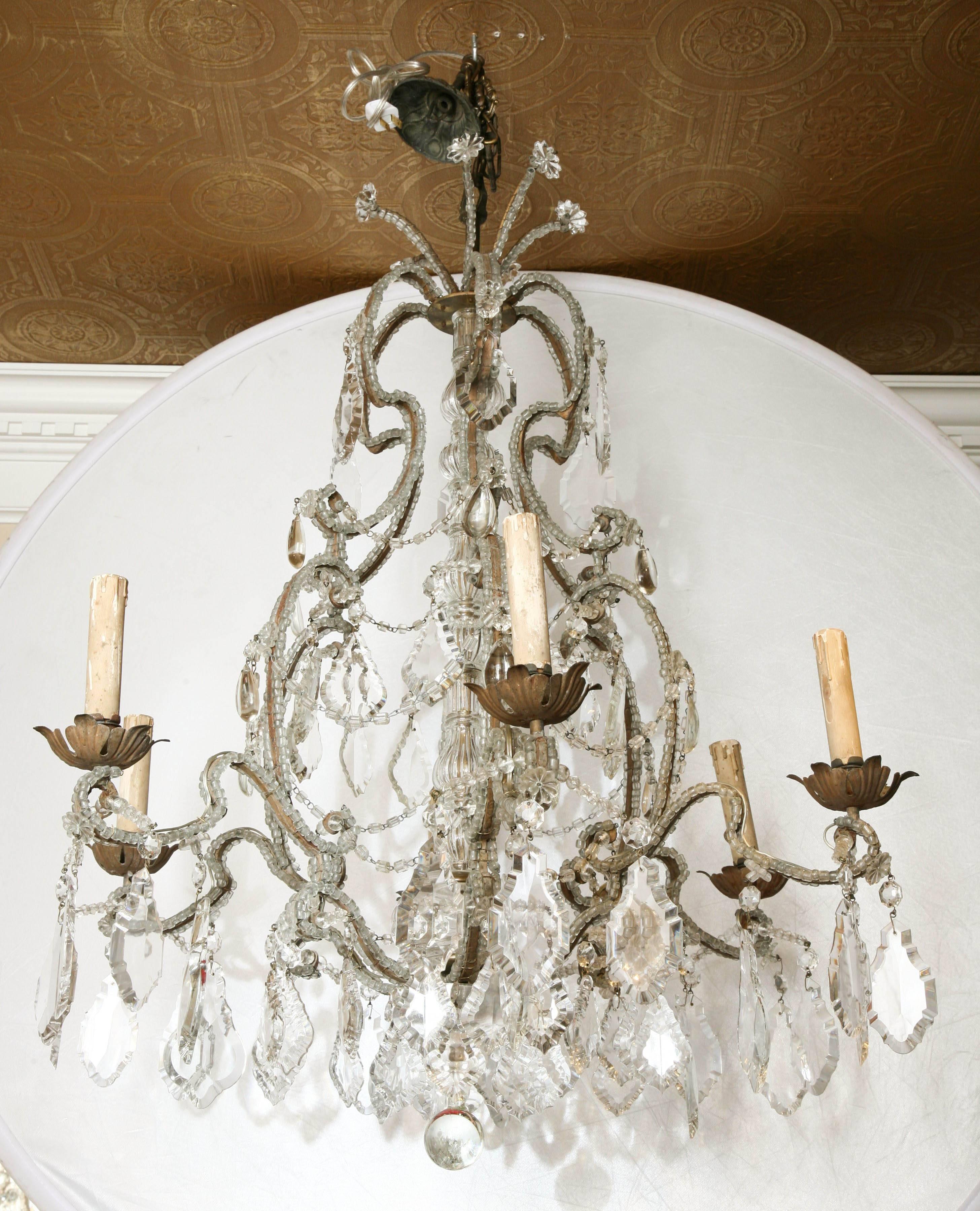 Chandelier, having a cage-form frame, of bronze, completely encrusted in macaroni glass beads, extruding six, scrolling candle arms, ending in foliate bobeches, surrounding its knopped glass central column, surmounted by a crown of "shooting