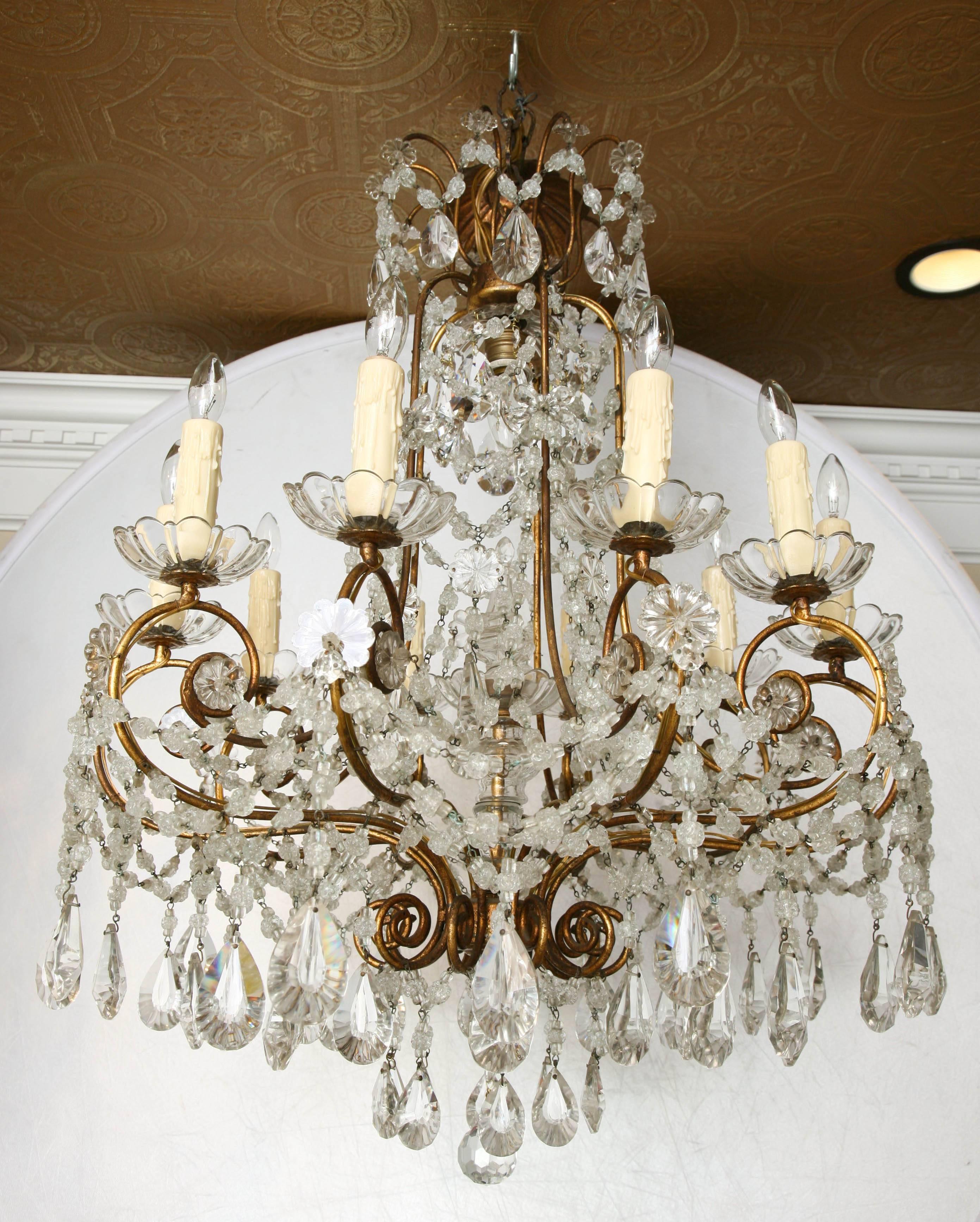Spectacular chandelier, having a cage-form frame of gilded iron, a handblown knopped glass spire sets inside the center, suspending ten S-scroll candle arms, each holding a scalloped bobeche and candle; surmounted by five upturned arms joining its