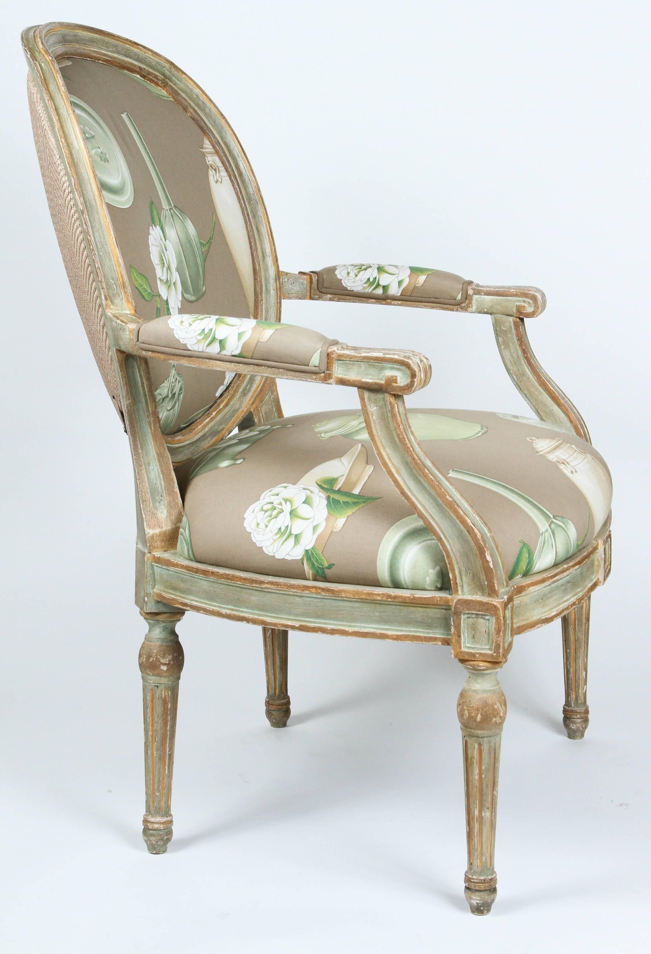 Pair of Louis XVI style oval-back armchairs upholstered in taupe, green cotton fabric with raffia fabric on backs. Wood painted green and cream with distressed finish.