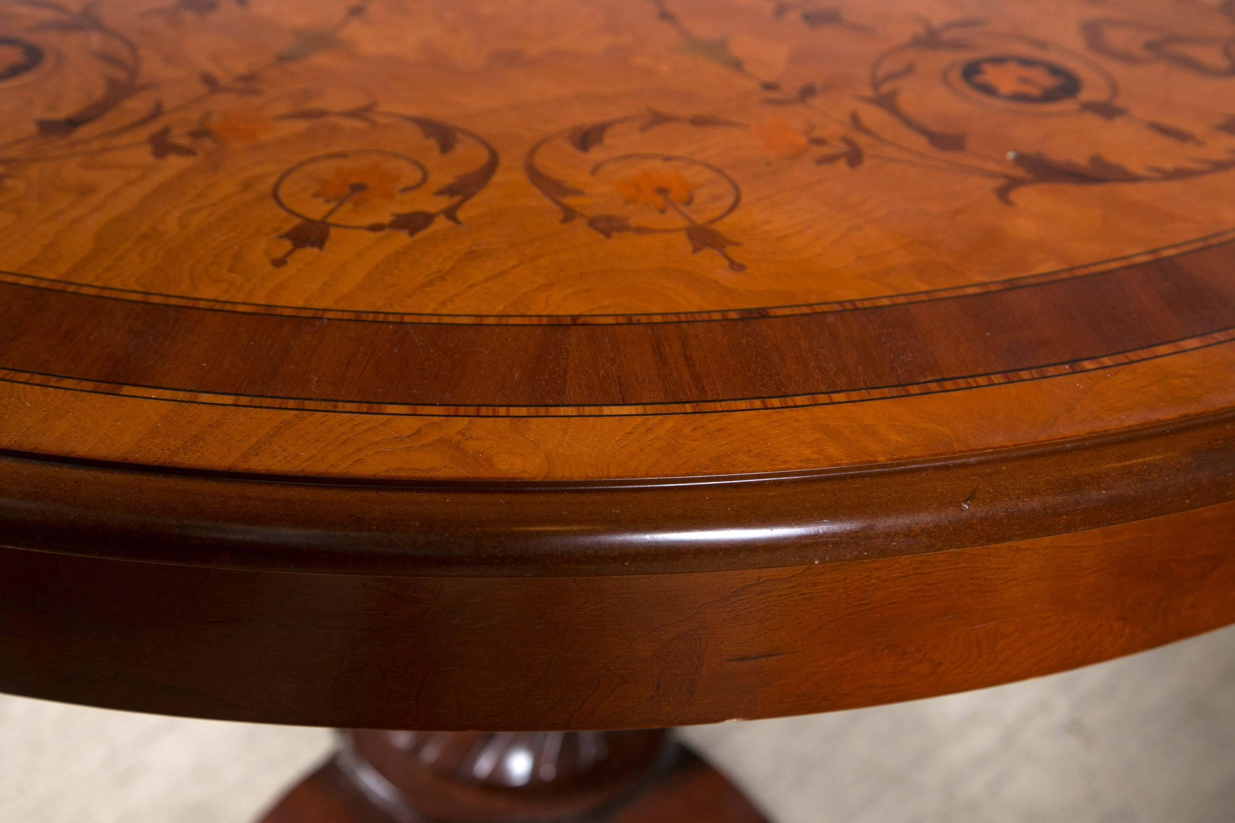 The round top, done in burl veneers, with inlaid outer band and borders, garlands, ribbons and flowers in mahogany, sycamore, walnut. Unusual pedestal with octagonal top, middle turning, swirled. On a four-scrolling and curled legs.