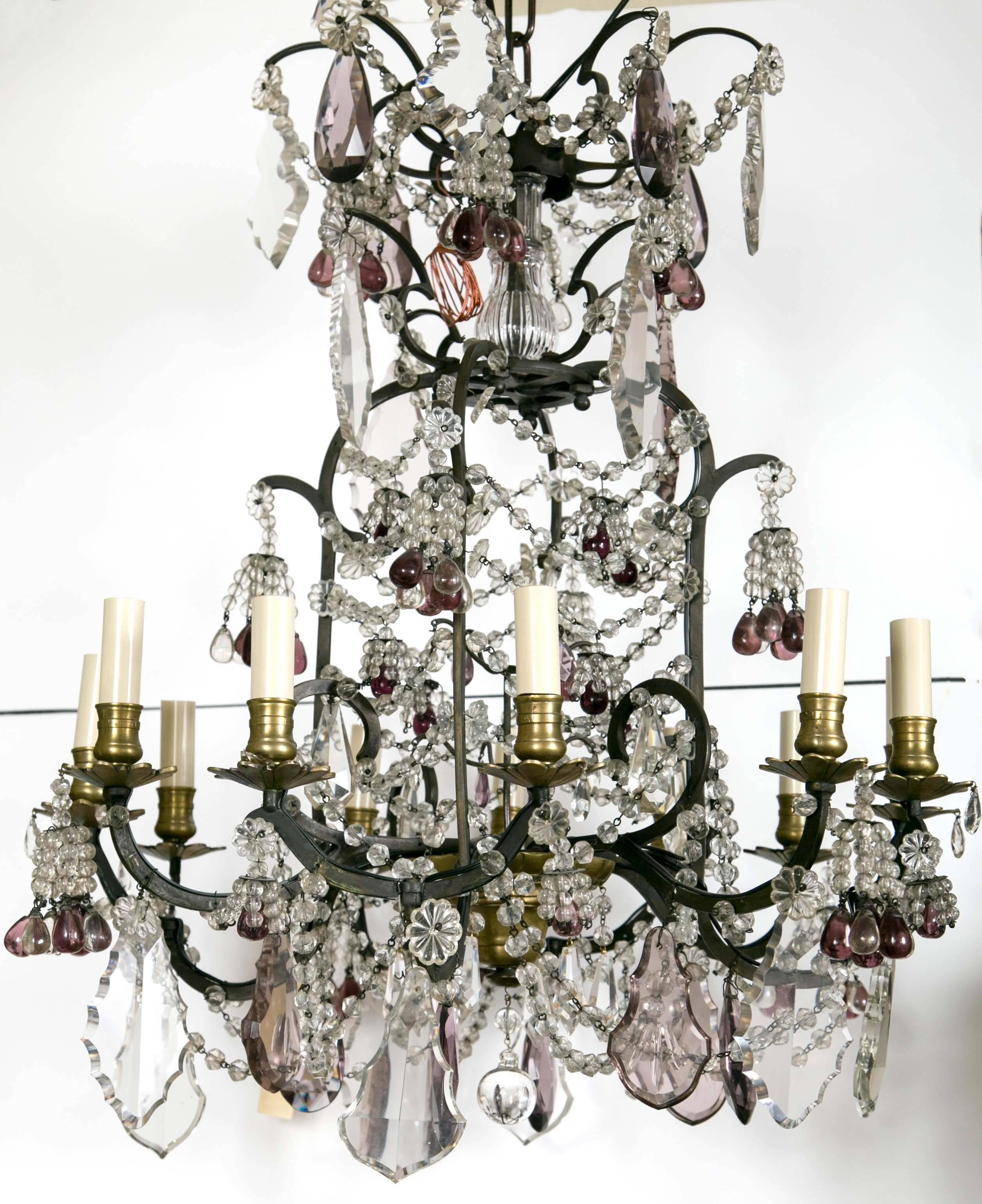 This chandelier is of iron with brass candle cups, baubeches and lower finial.
Each arm (six) projects from the cage and each has two arms which carry the lights. The wiring in outside of the arms.
Clear and pale lavender glass drops of varying