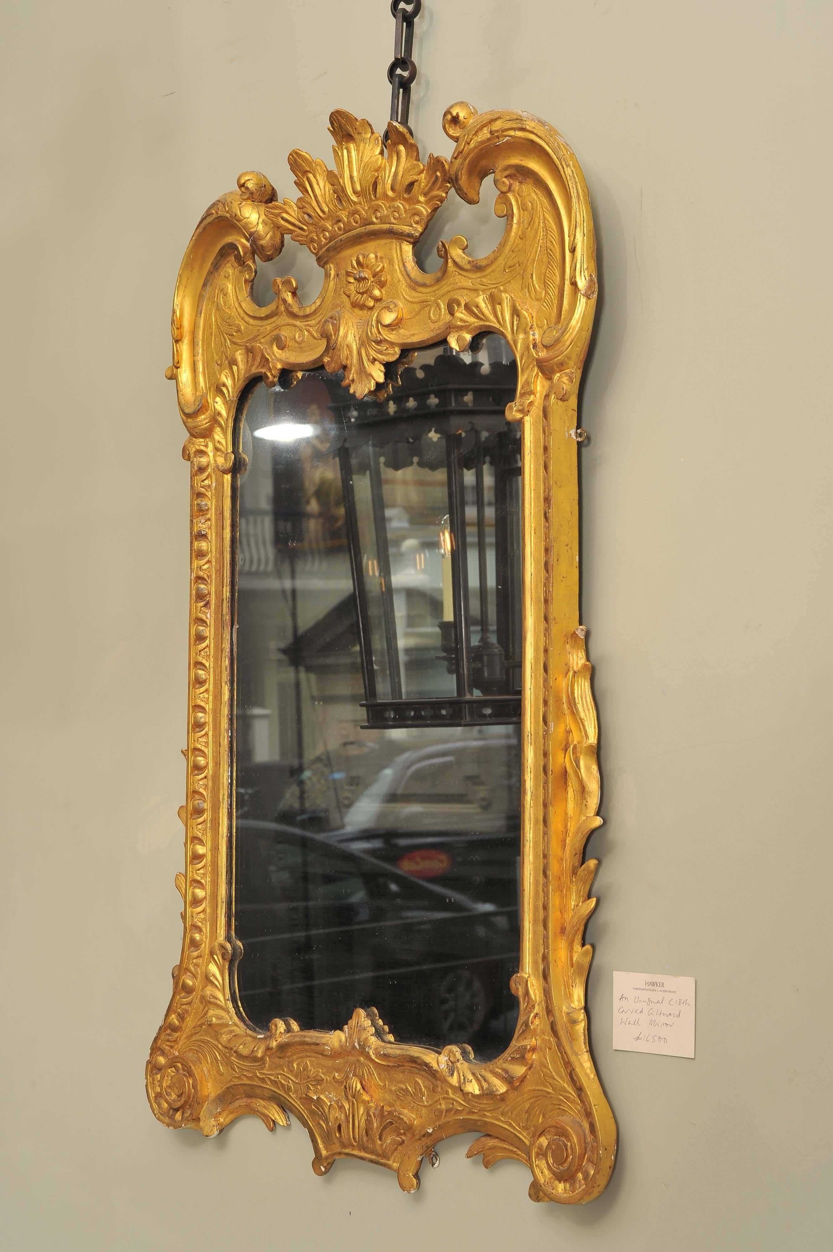 Miroir mural inhabituel en bois doré sculpté du XVIIIe siècle, avec fronton en arc de cercle surmonté d'une couronne et de volutes en C au-dessus d'une plaque rectangulaire entourée d'un cadre décoré de feuilles raides et d'acanthes,
vers 1740,