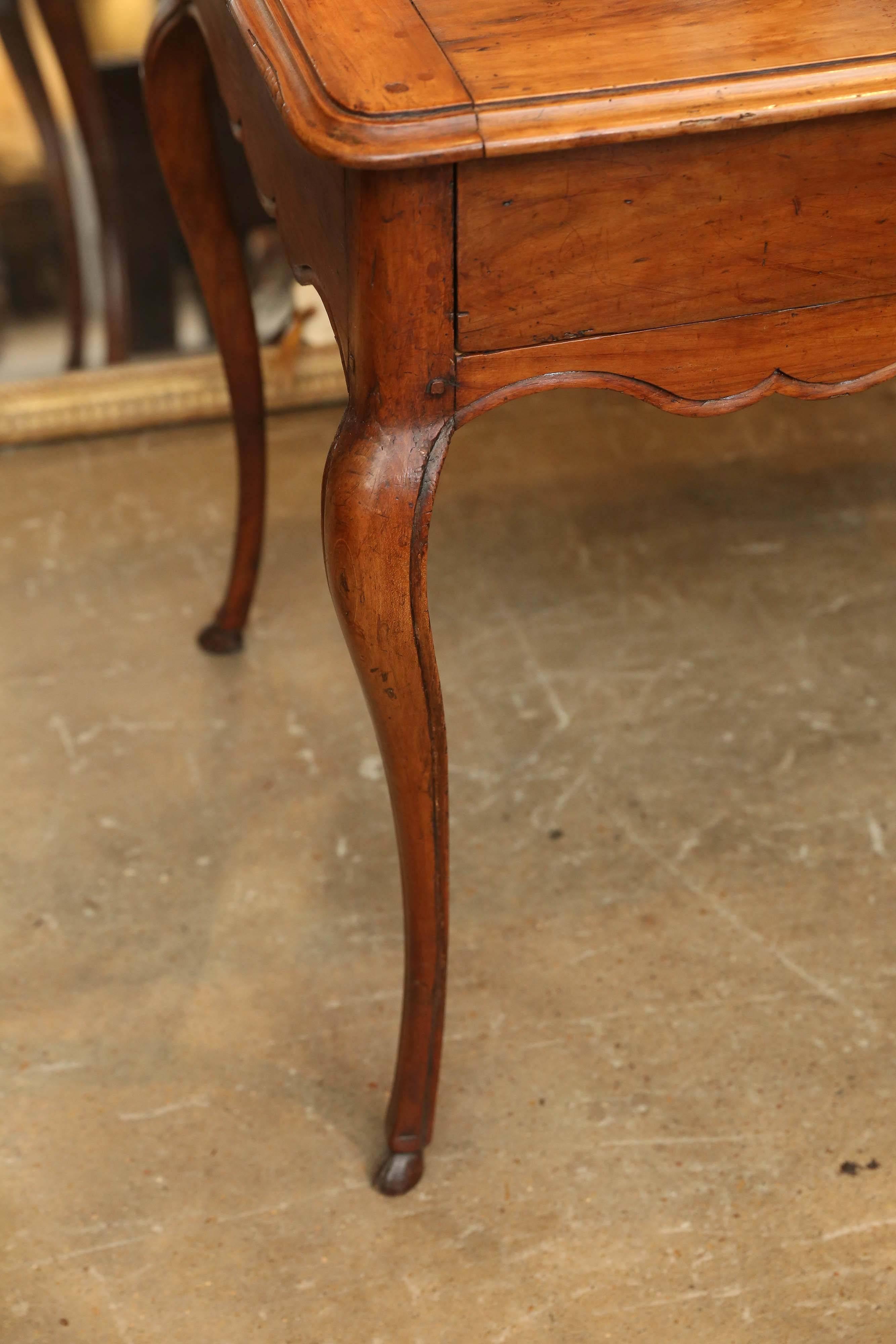 18th Century Louis XV period cherry wood table with a large front drawer. Beautiful delicate cabriole legs end in a carved animal hoof detail. The apron of the table has a soft curves accentuated by a carved detail that starts at the base of each