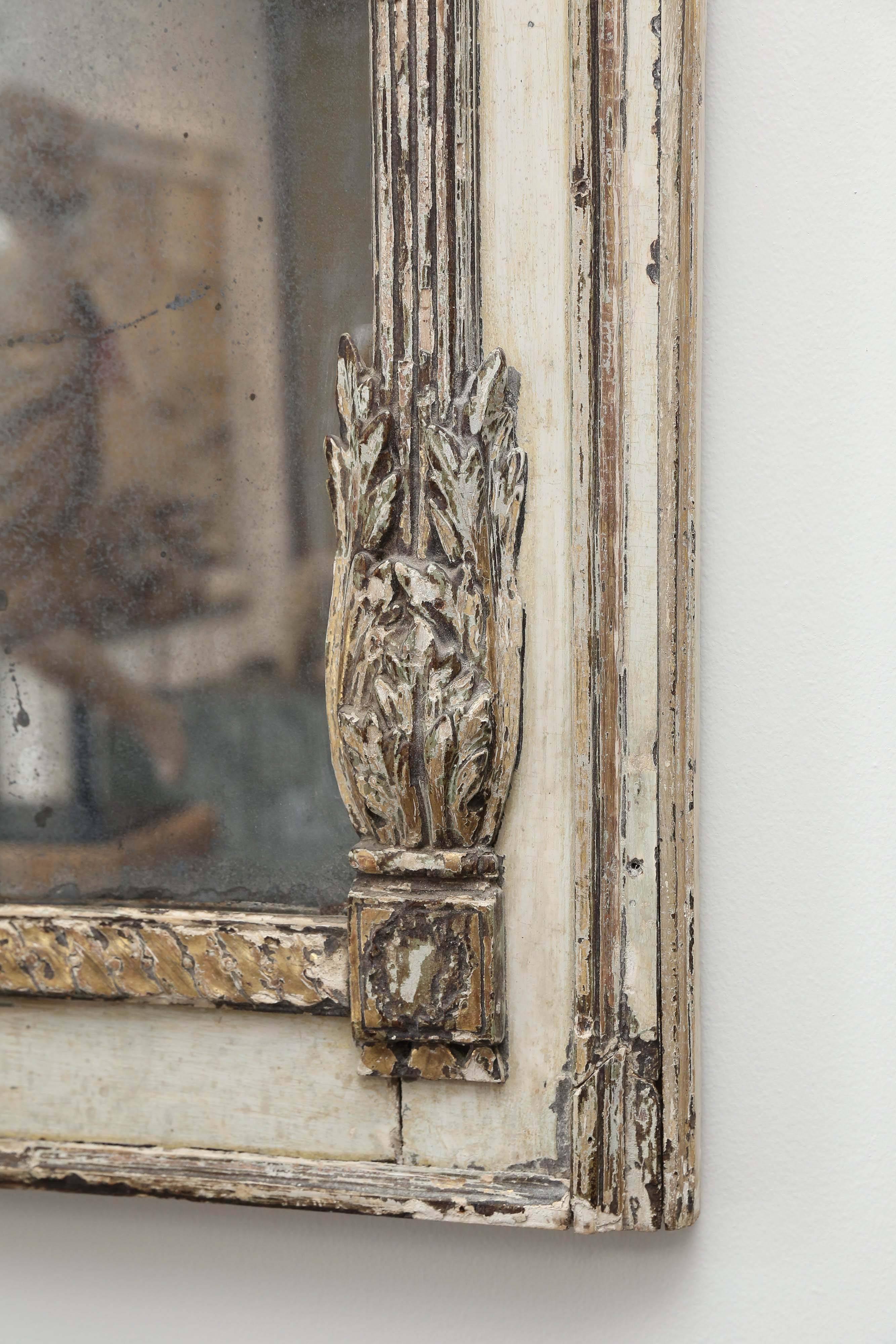 19th century French Trumeau with traces of gilt and silver throughout the carved wooden detail. The mirror's frame is flanked by two reeded columns with pineapple like finials at the top and a swag detail below the columns' capitals. At the opposite