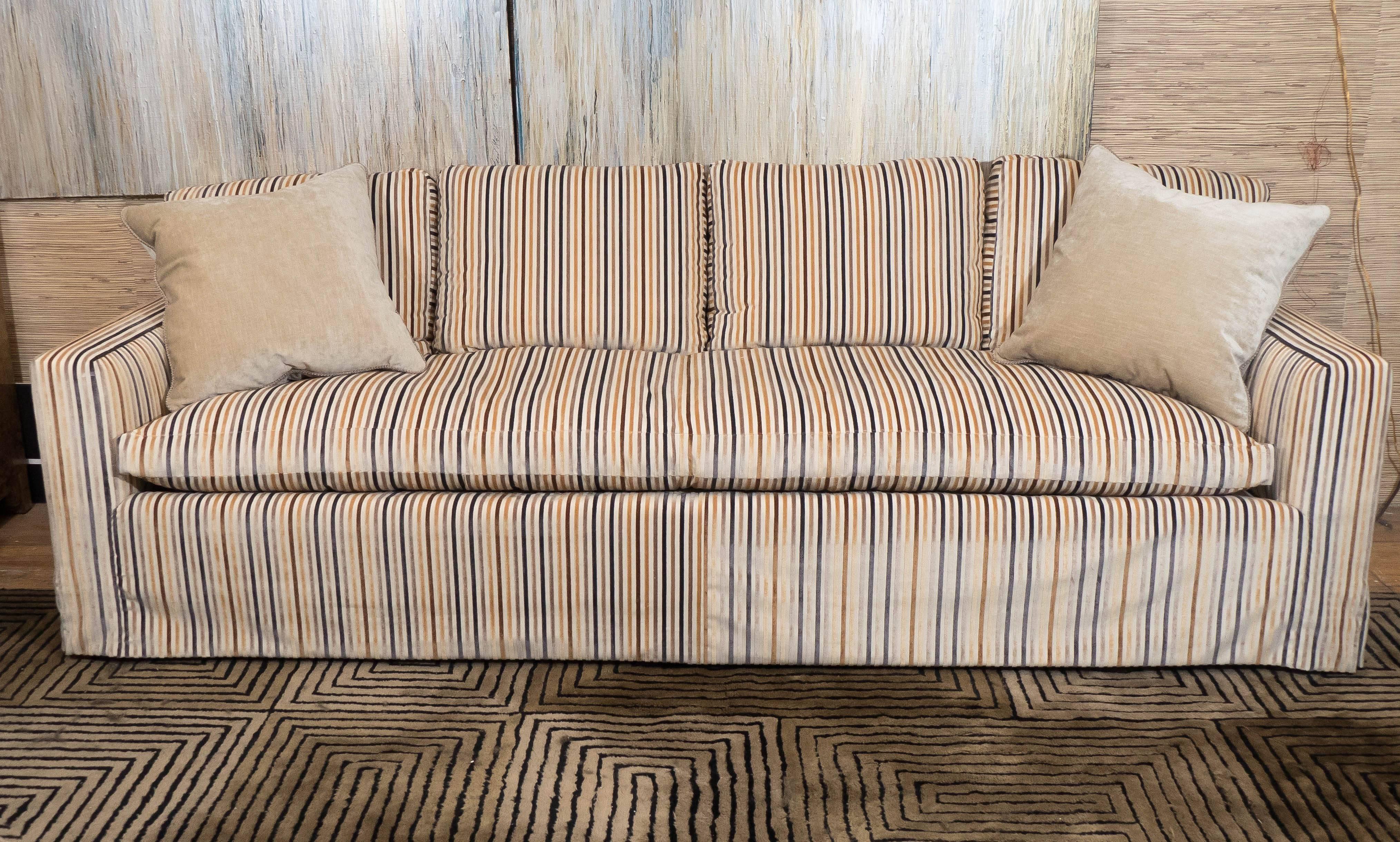 This down sofa, produced circa 1960s, comes upholstered in striped cut velvet, with track arms and bench seat. Very good vintage condition, consistent with age and use.