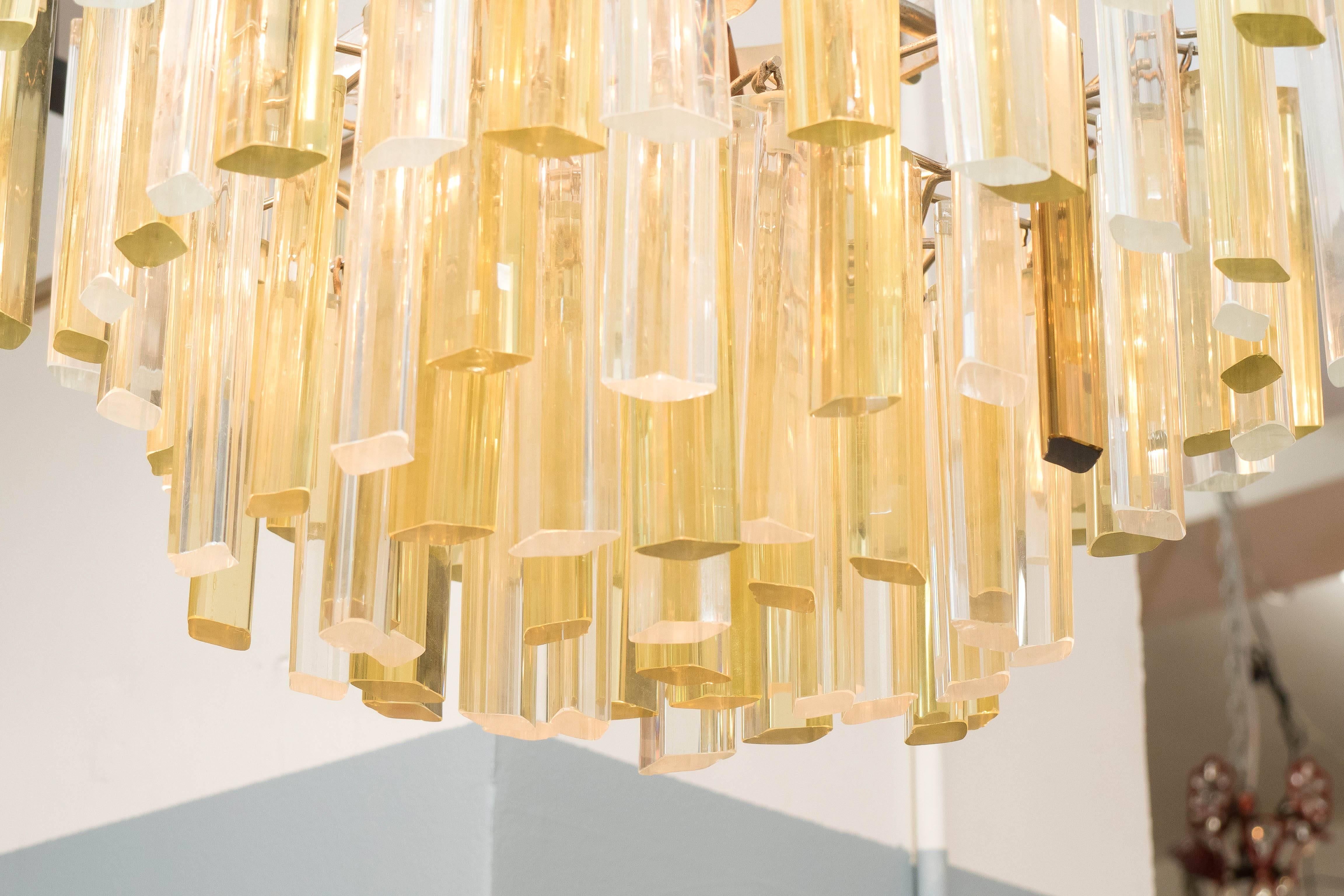 A chandelier by Venini, produced circa 1970s, with three tiers of suspended glass prisms, in clear and gold tones. Requires four candelabra base bulbs. This light fixture remains in very good condition, with no loss of prisms or presence of damage