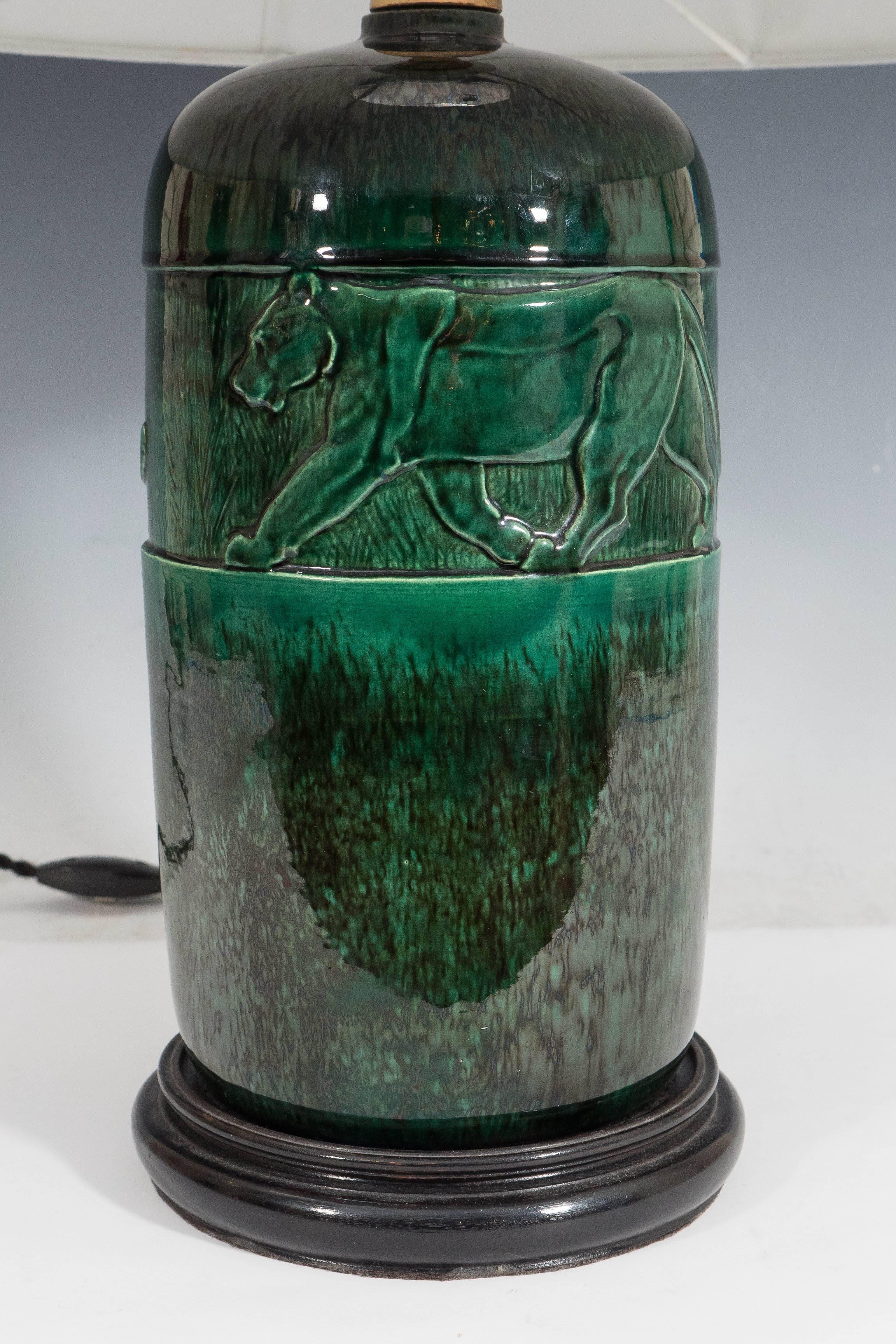 This French Art Deco era table lamp, produced circa 1920s by René Meynial, comes with bayonet socket on green glazed ceramic body, with detail of a prowling panther, mounted on a black wooden base; black twisted cord with on/off switch included.