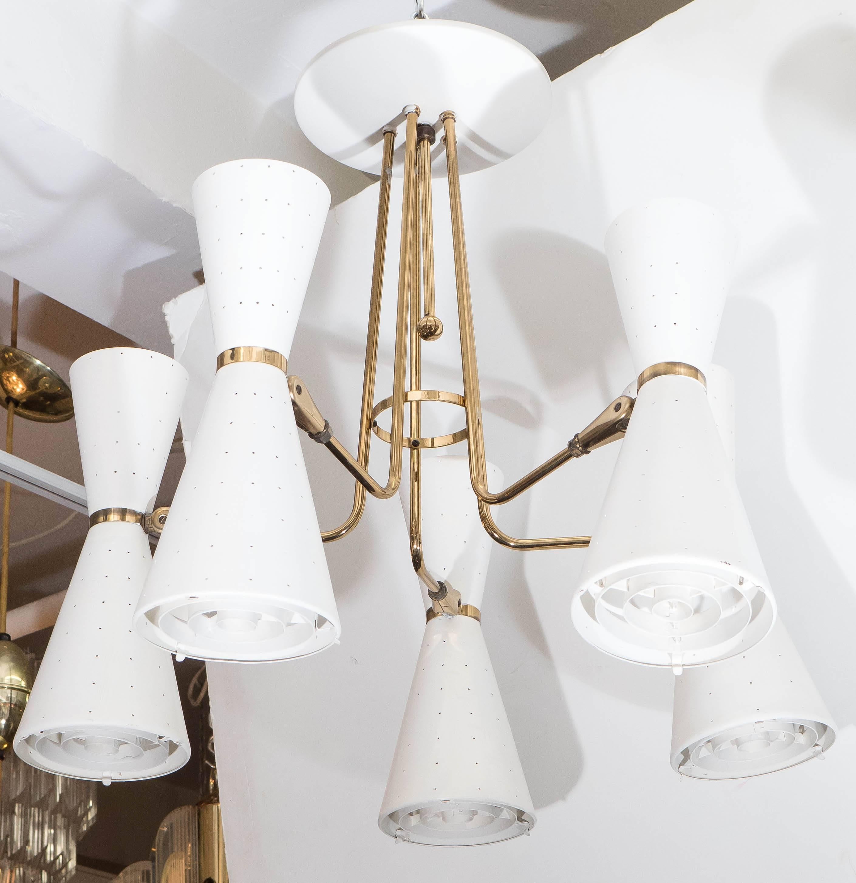 A Lightolier chandelier, produced circa 1960s, with five curved brass arms, each supporting dualistic, white painted conical shades with perforated detail and diffusers, suspended from a saucer form canopy. Requires ten medium base bulbs. This light