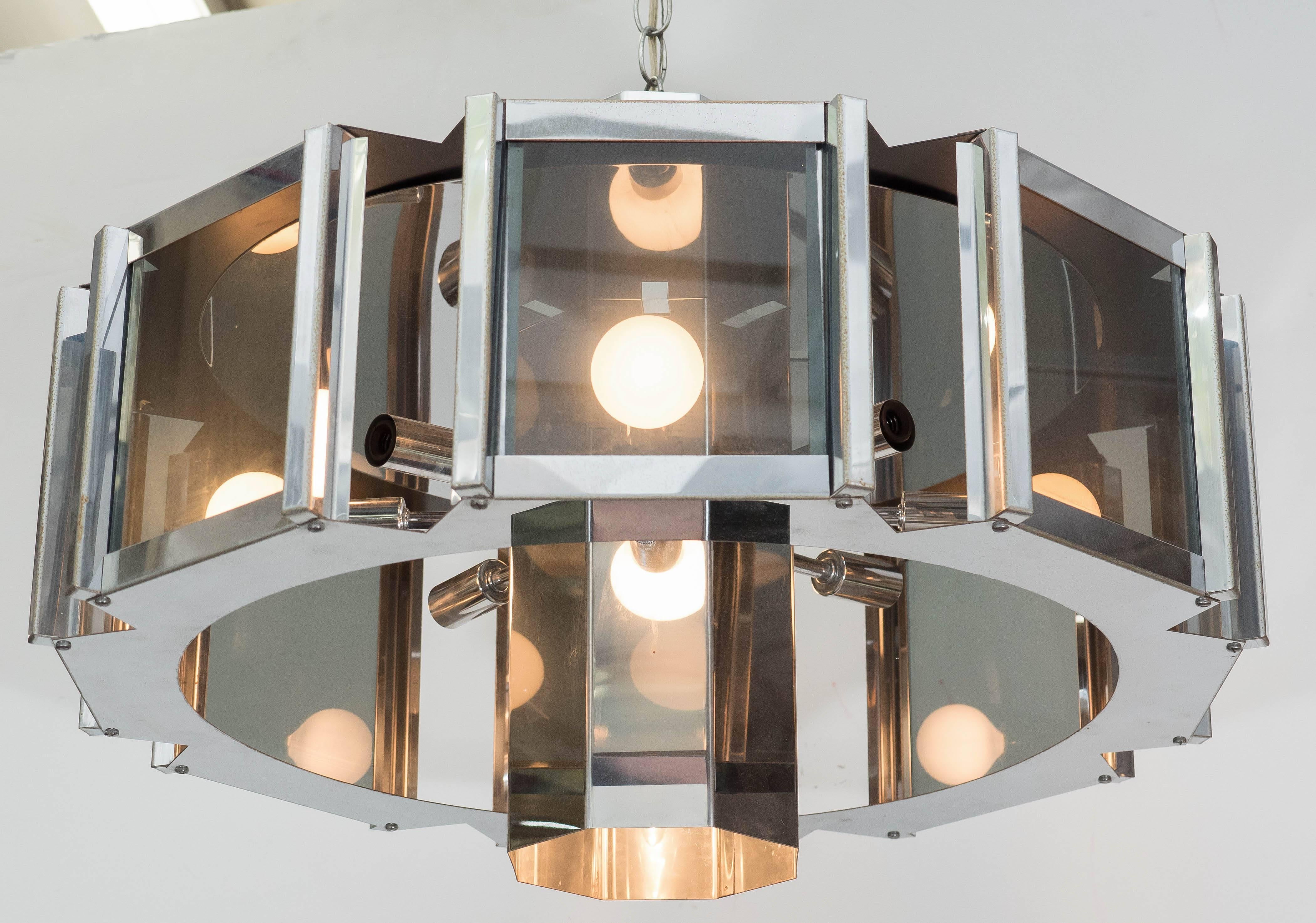 A octagonal chandelier by designer Frederick Ramond, with sockets and reflective cylindrical nucleus echoing the surrounding eight sided chrome frame, inset with smoked glass panels, circa 1980s. This light fixture is in very good condition,