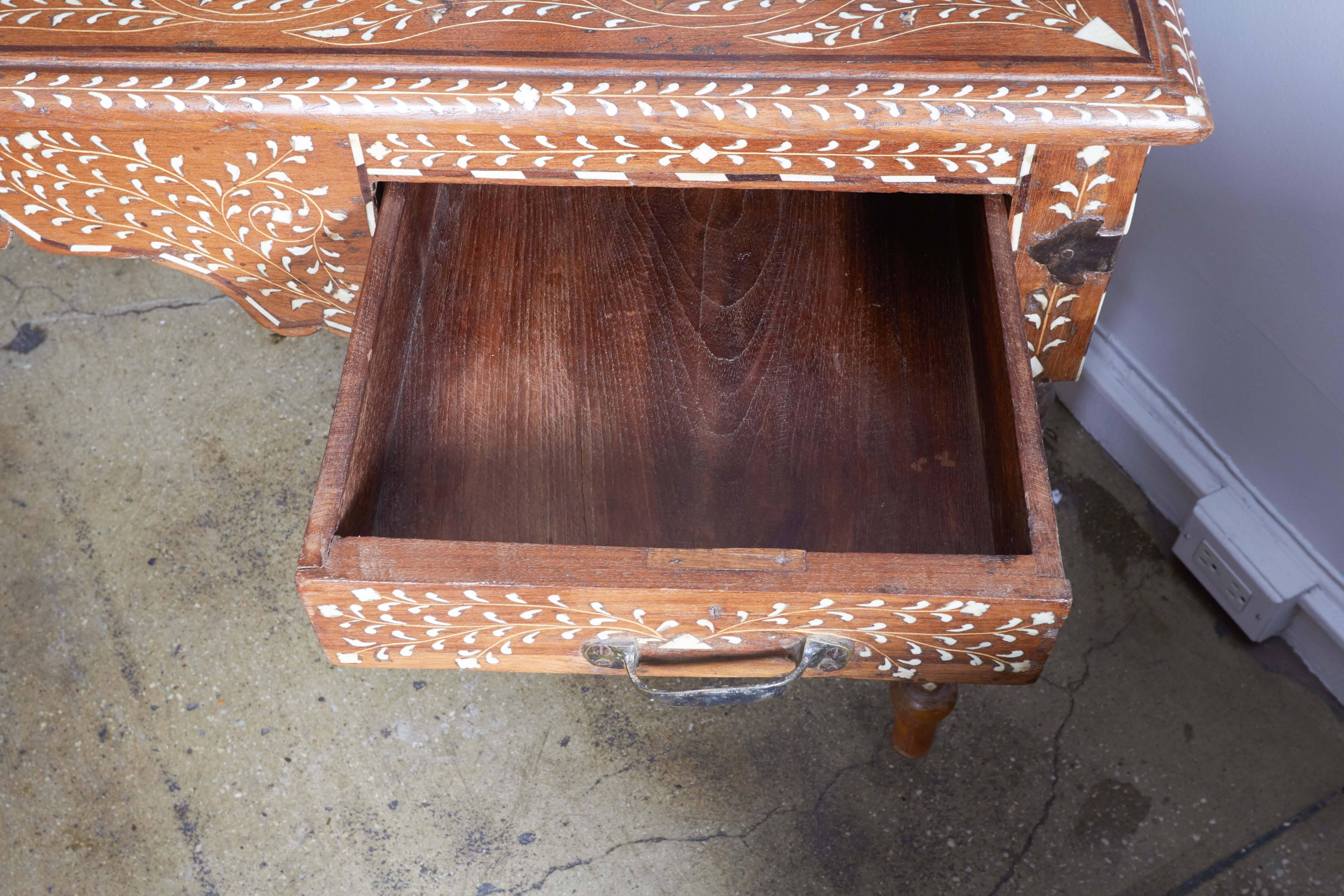 A large desk with two drawers, turned legs and bone inlay in a Classic pattern on all sides, from India. Brass handles and corner trim.