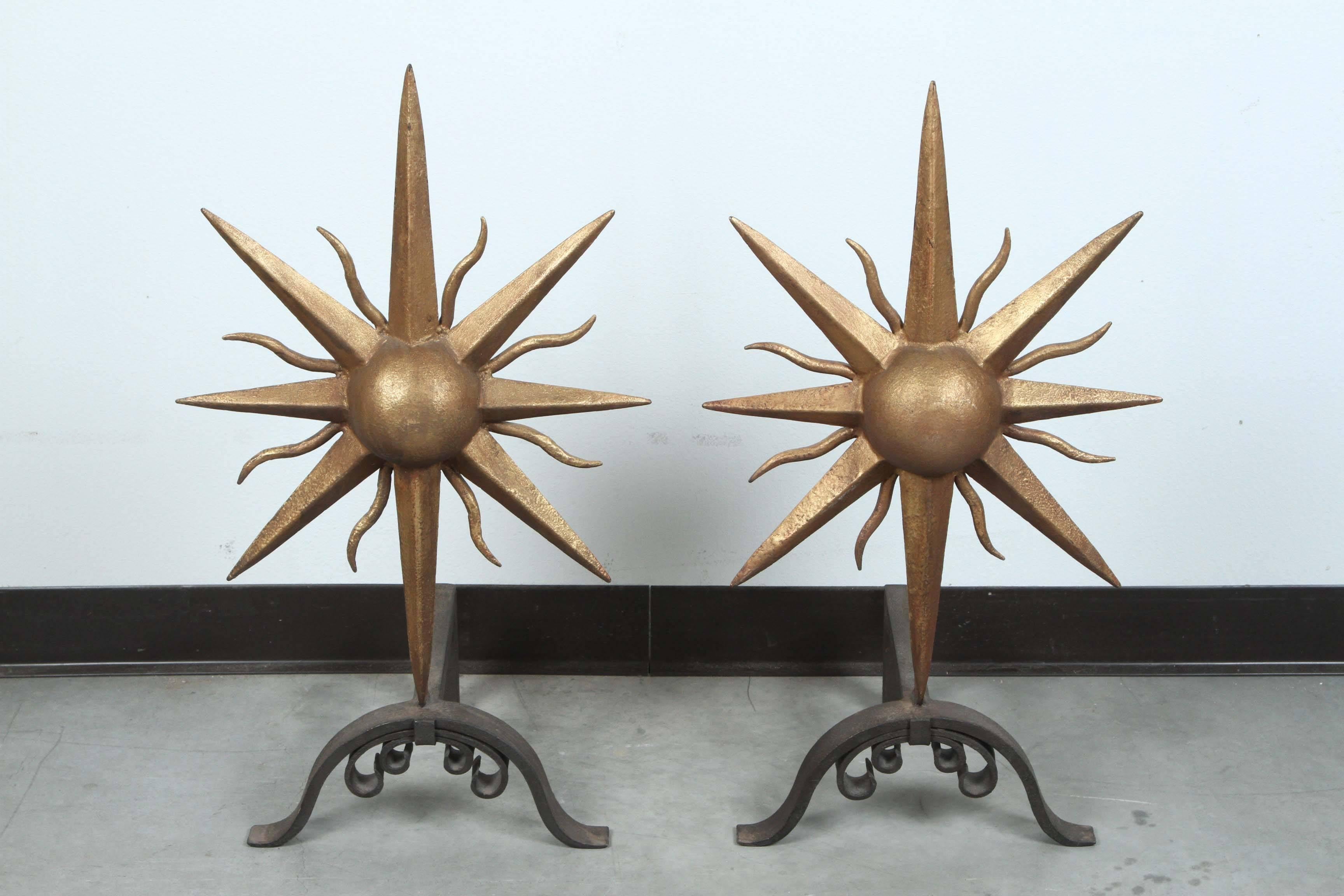 Great pair of andirons with a sunburst design. 
The large cast iron sunbursts have a dull gold finish and they are on black wrought iron bases.