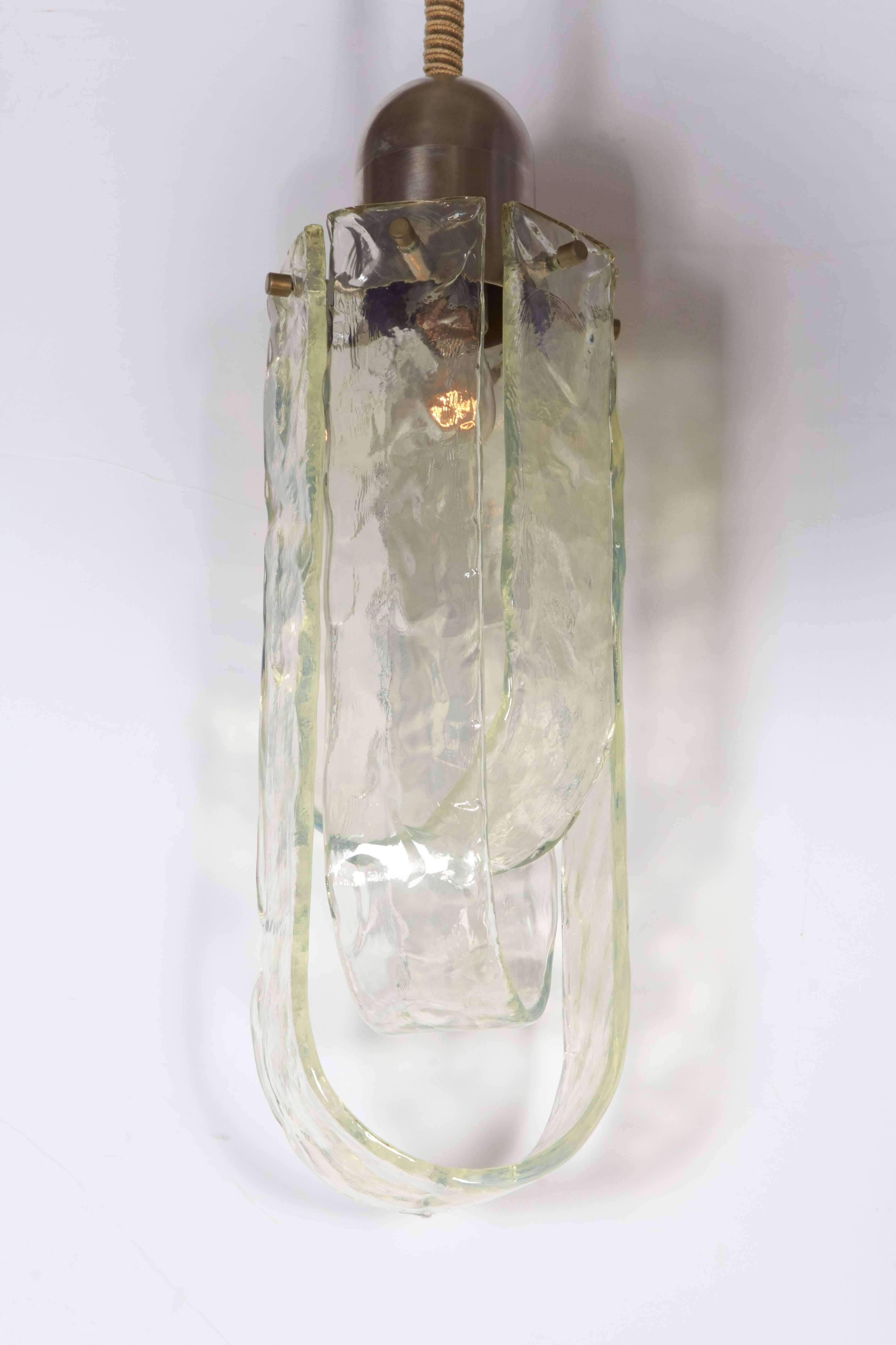 A lovely 1970s modern design pendant light by well-known Italian lighting and glass house Mazzega. Three wide hand formed long bands of glass in small, medium and large sizes are suspended over a single light bulb. The glass bands create a shade