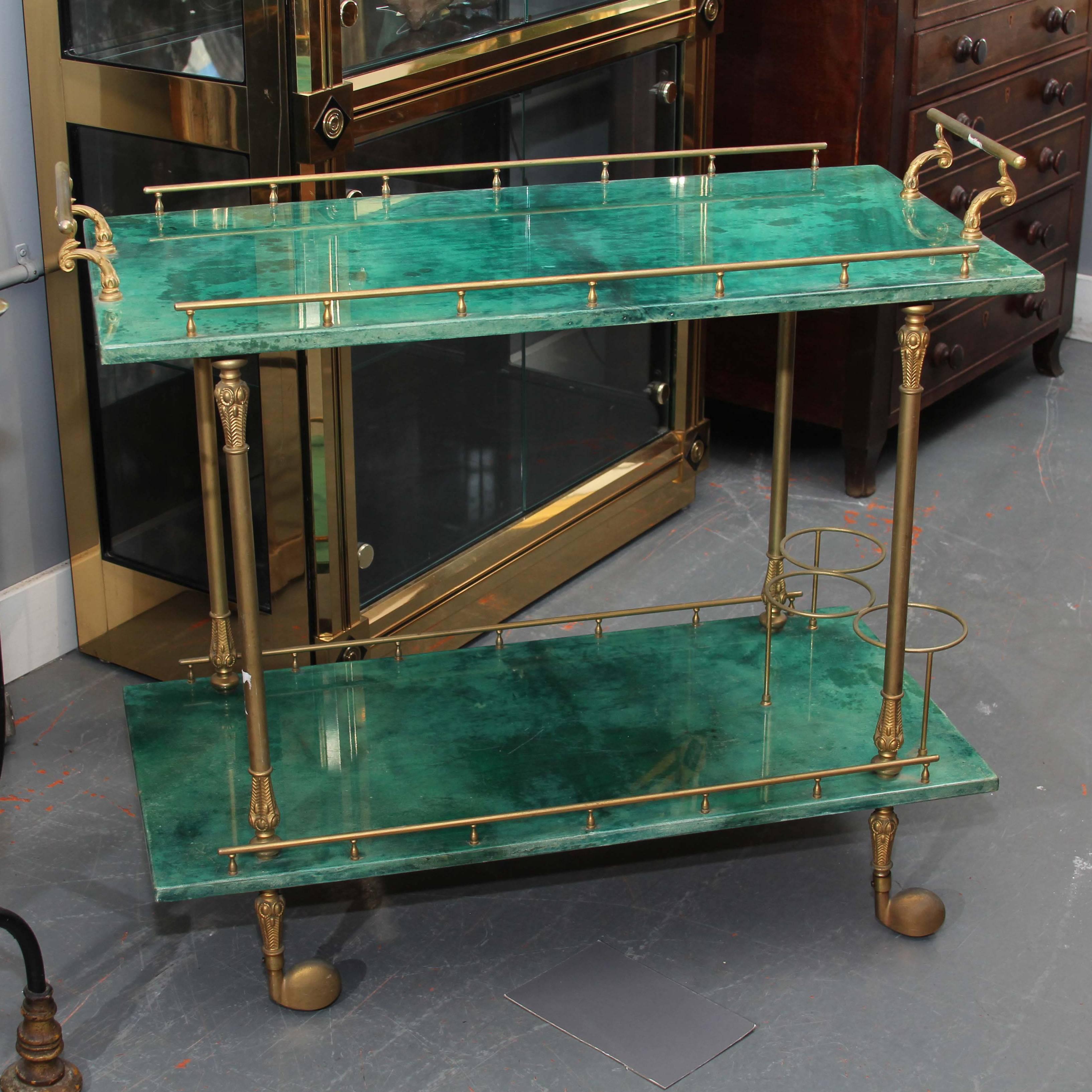 Two-tier bar cart in lacquered emerald green goatskin with brass detail including handles and top and bottom fencing with circular bottle holders, Italy.