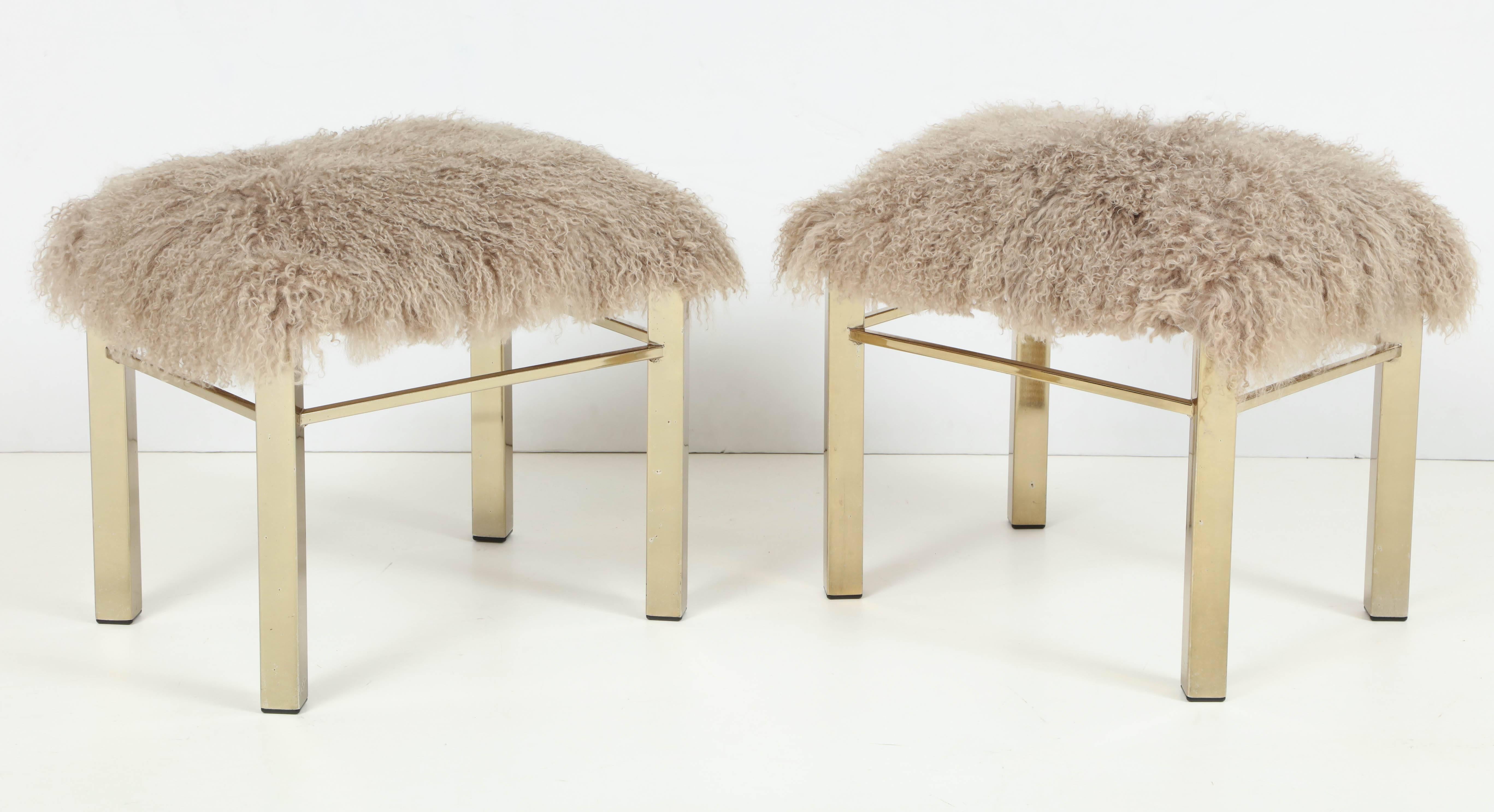 Wonderfully elegant and chic matching pair of brass-plated steel stools or benches. Newly upholstered in silky taupe or beige colored long haired Argentine Mongolian goat hide. 

This pair of stools is on display at the 1stdibs showroom at the New