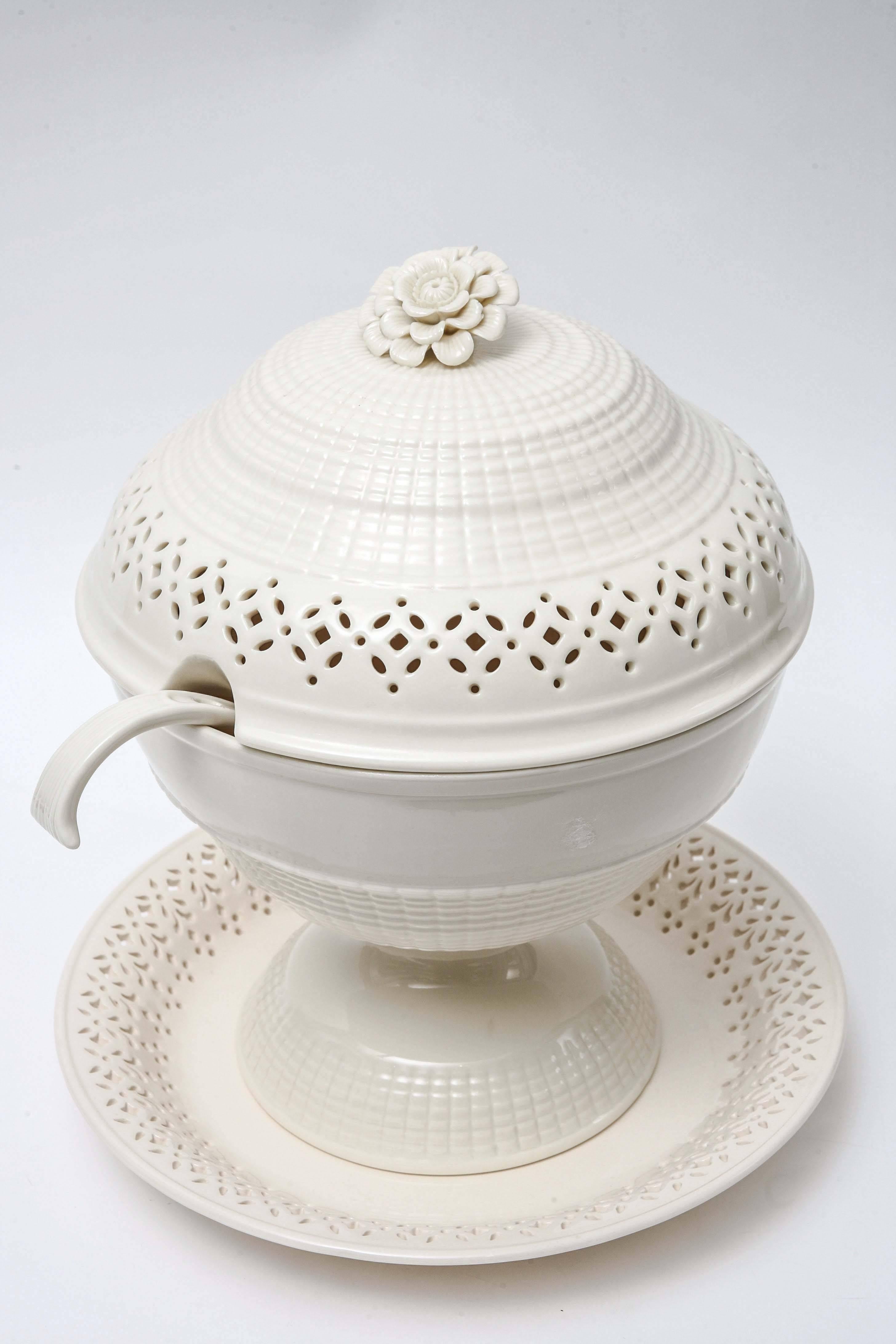 A large pedestal base cream ware tureen that features hand cut work, a lovely detailed floral topped finial. Complete with its ladle and undertray this stunning piece would work well as a centerpiece as well as anchor a display. A newer piece in