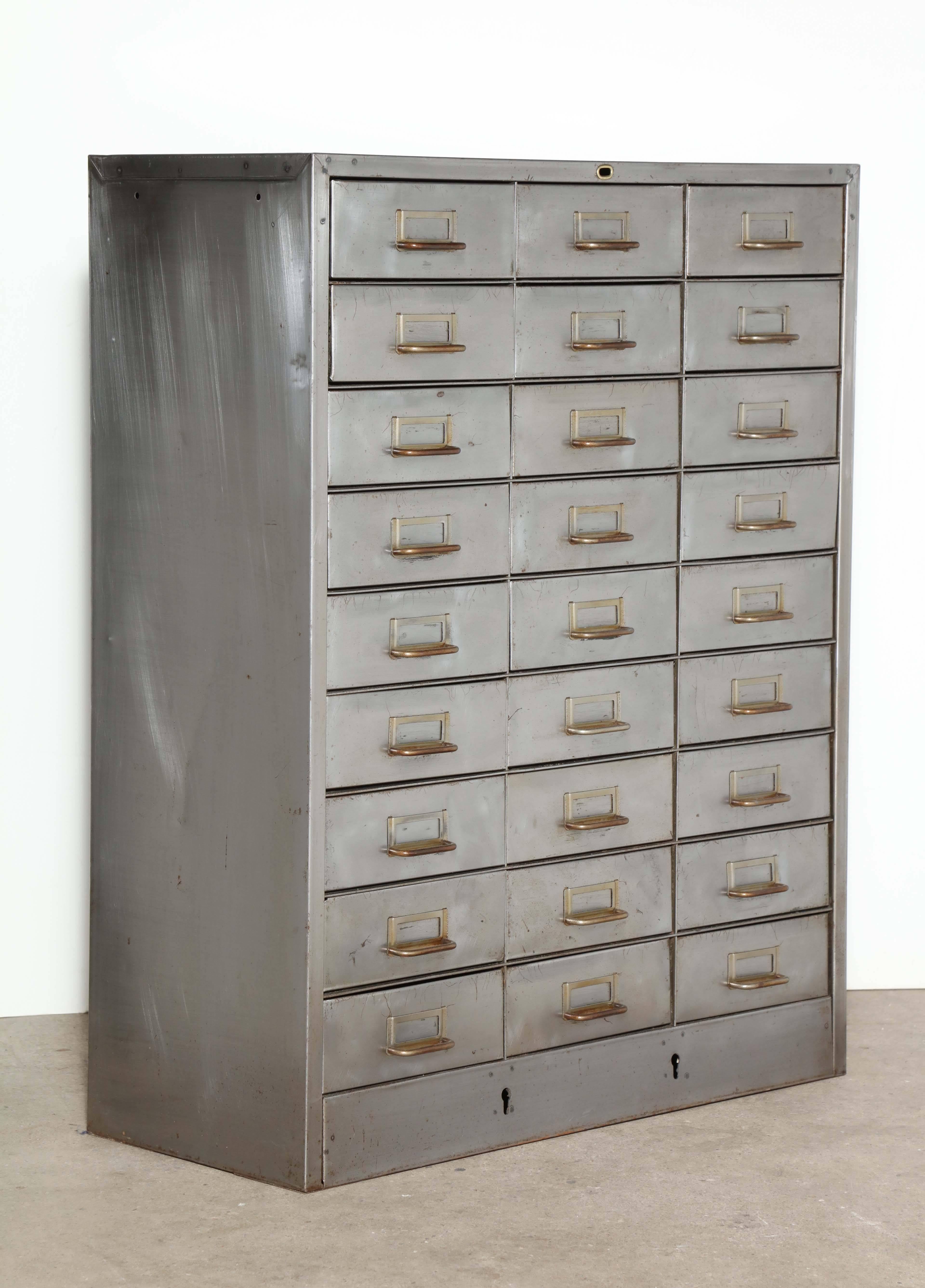 27 drawer, Apothecary style, steel and brass storage cabinet, circa 1940s,
with brass name plates and drawer pulls. Great storage for smaller parts. 
Three rows of nine drawers each. Drawer dimensions: 9