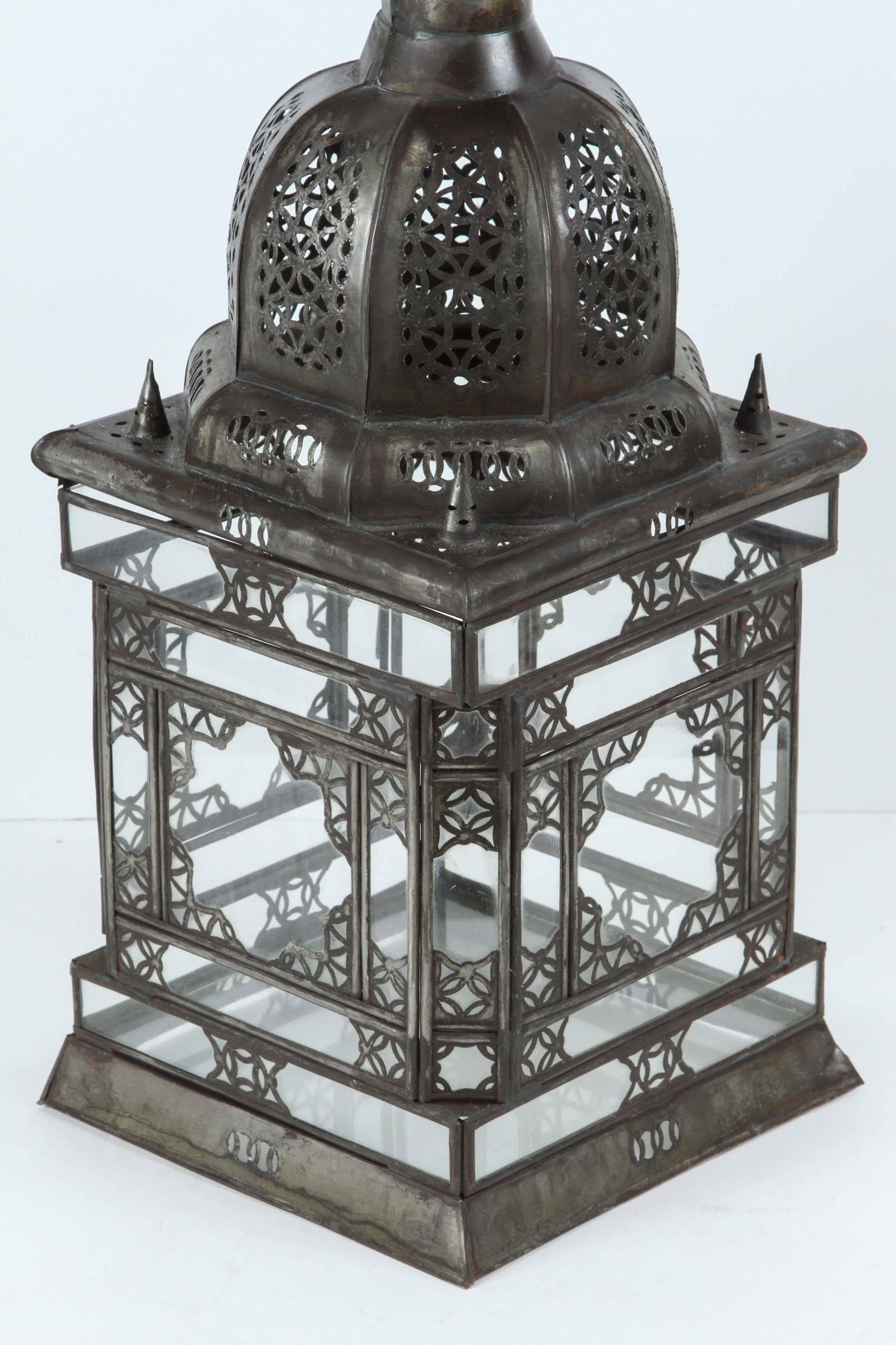 Moroccan Moorish clear glass candle lantern with filigree designs, handcrafted in Morocco. Rust patina color finish.
Hurricane candle lamp with clear glass bottom, great to use as a table lantern or hanging pendant or wall sconce.
The lantern has a
