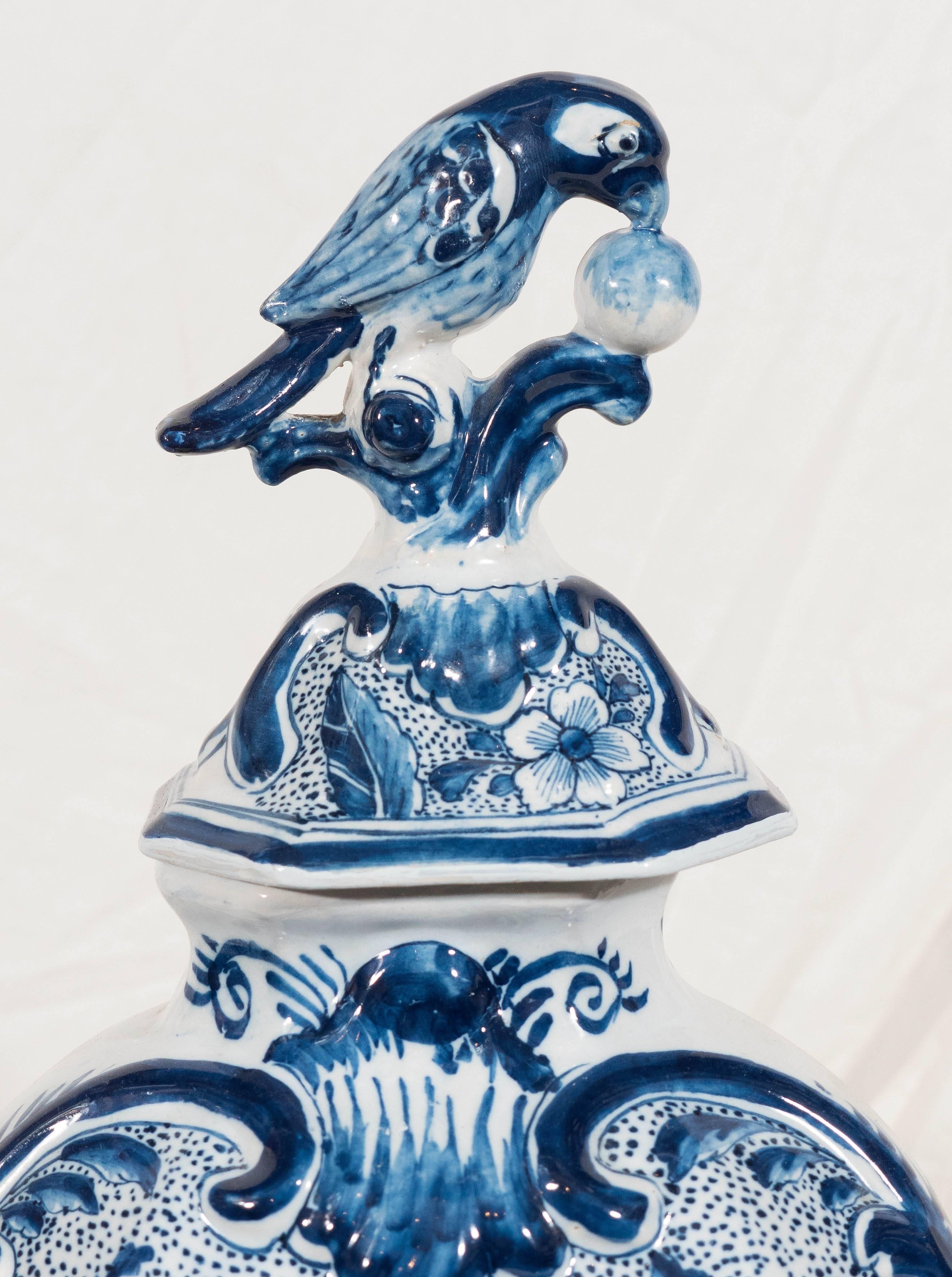 A Dutch Delft Blue and White covered vase decorated with a bouquet of flowers
on a blue speckled ground. The cover is topped by a traditional bird and ball
finial. The back of the vase is decorated with a single Artemisia leaf.
We feel that this