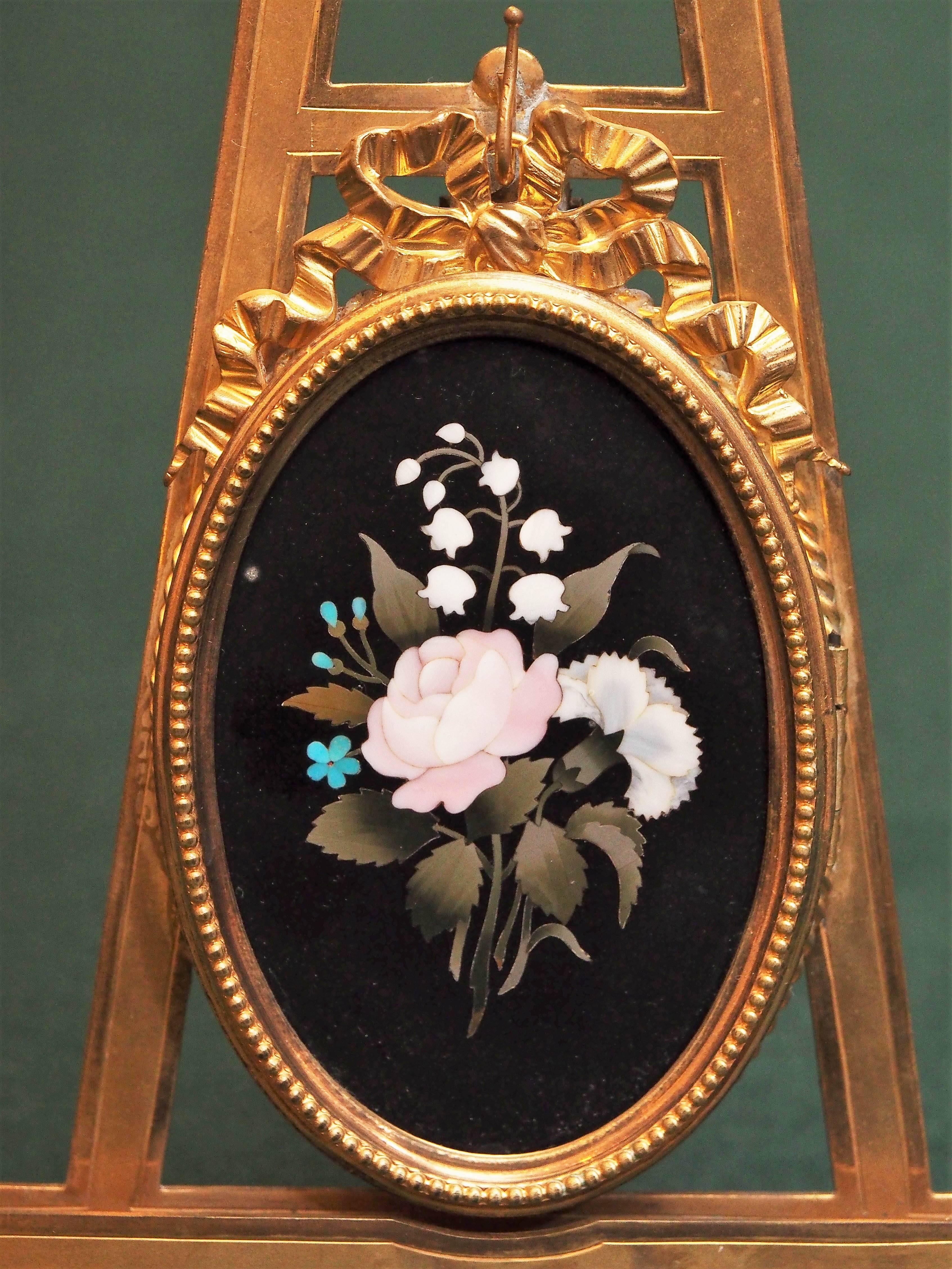Italian Pietra Dura plaque with gilt bronze frame on gilt bronze easel.
The oval plaque is surrounded by a Napoleon III style oval bow mounted frame that opens to reveal a space for a photograph. Easel back allows freestanding.
   