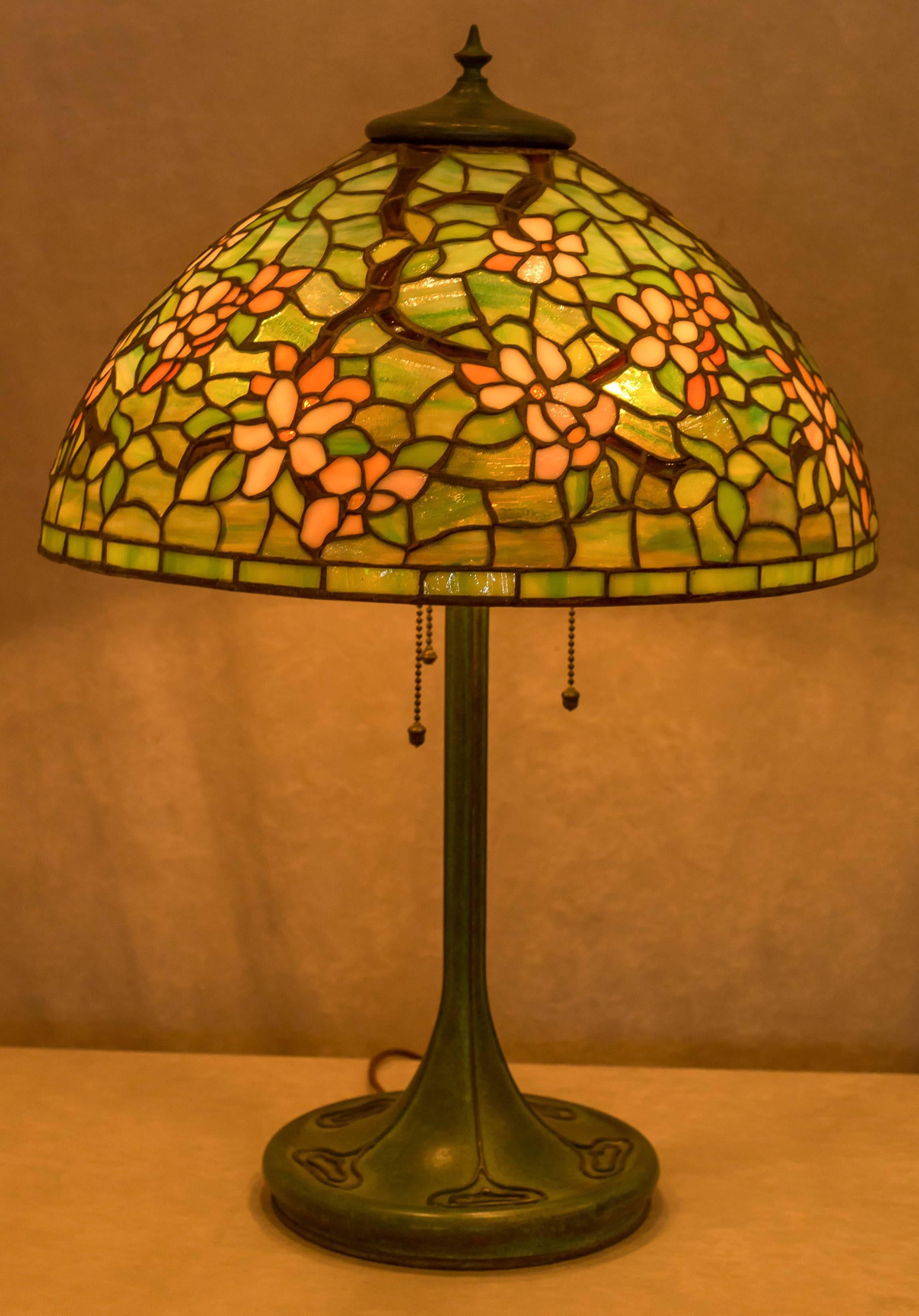 This very colorful and well designed leaded glass lamp was done by The Unique Art Glass Company, which made some of the finest leaded glass lighting and was the first to follow Tiffany. The spun bronze base is highlighted by their beautiful