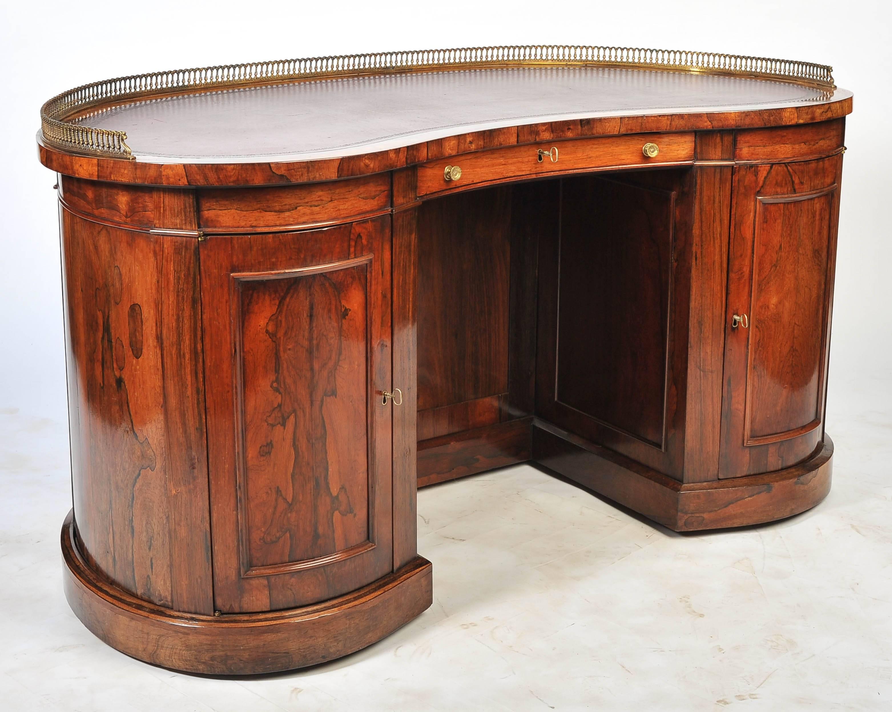 A good quality late Regency period rosewood kidney shape pedestal desk, having a three quarter brass gallery, an inset leather top. Three frieze drawers, the central one having a hinged leather reading slope, two cupboard doors opening to reveal