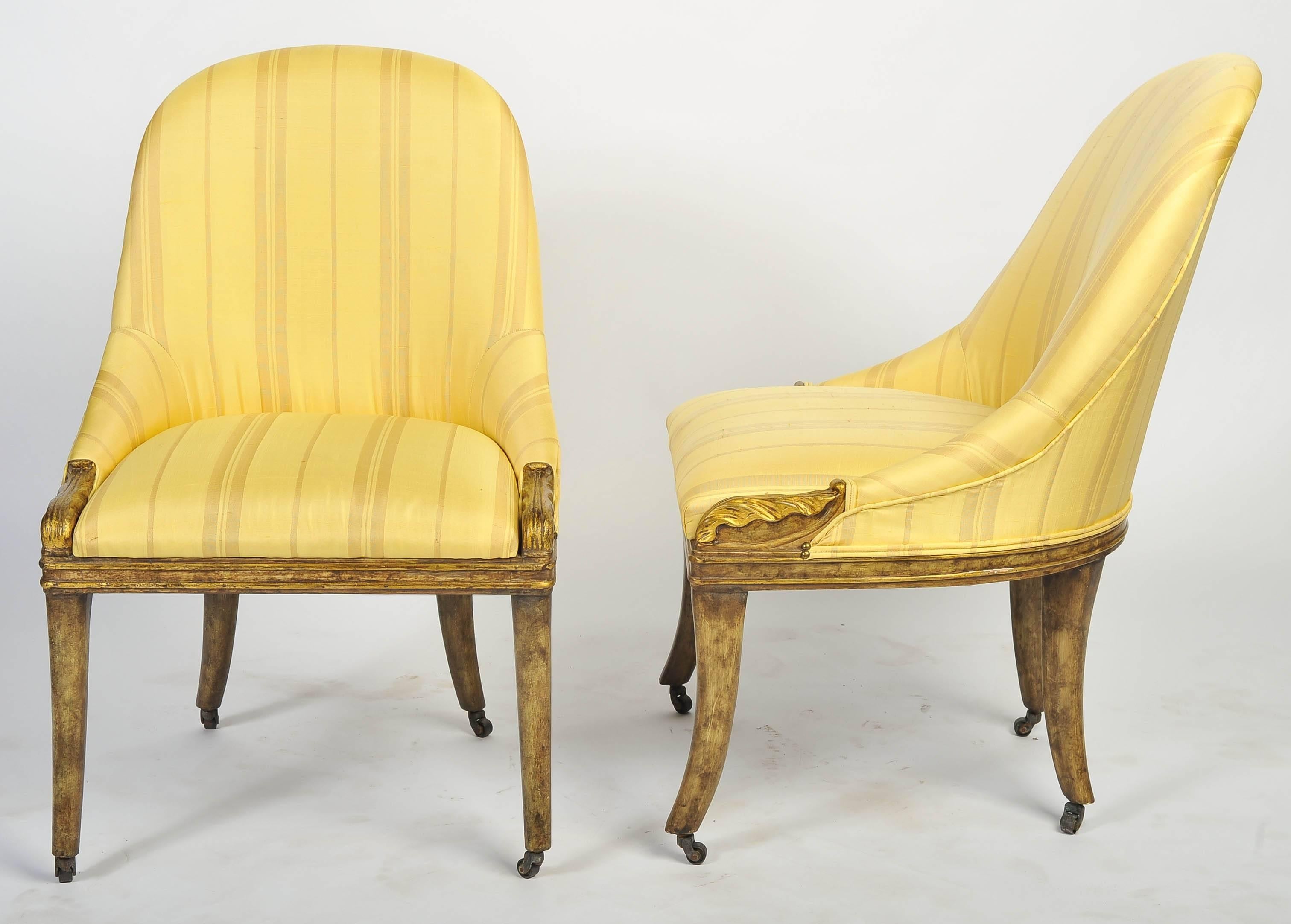A very stylish pair of cream painted Regency slipper side chairs, having stuff over upholstery, carved scrolls to either side and raised on out swept sabre legs, terminating in brass castors.