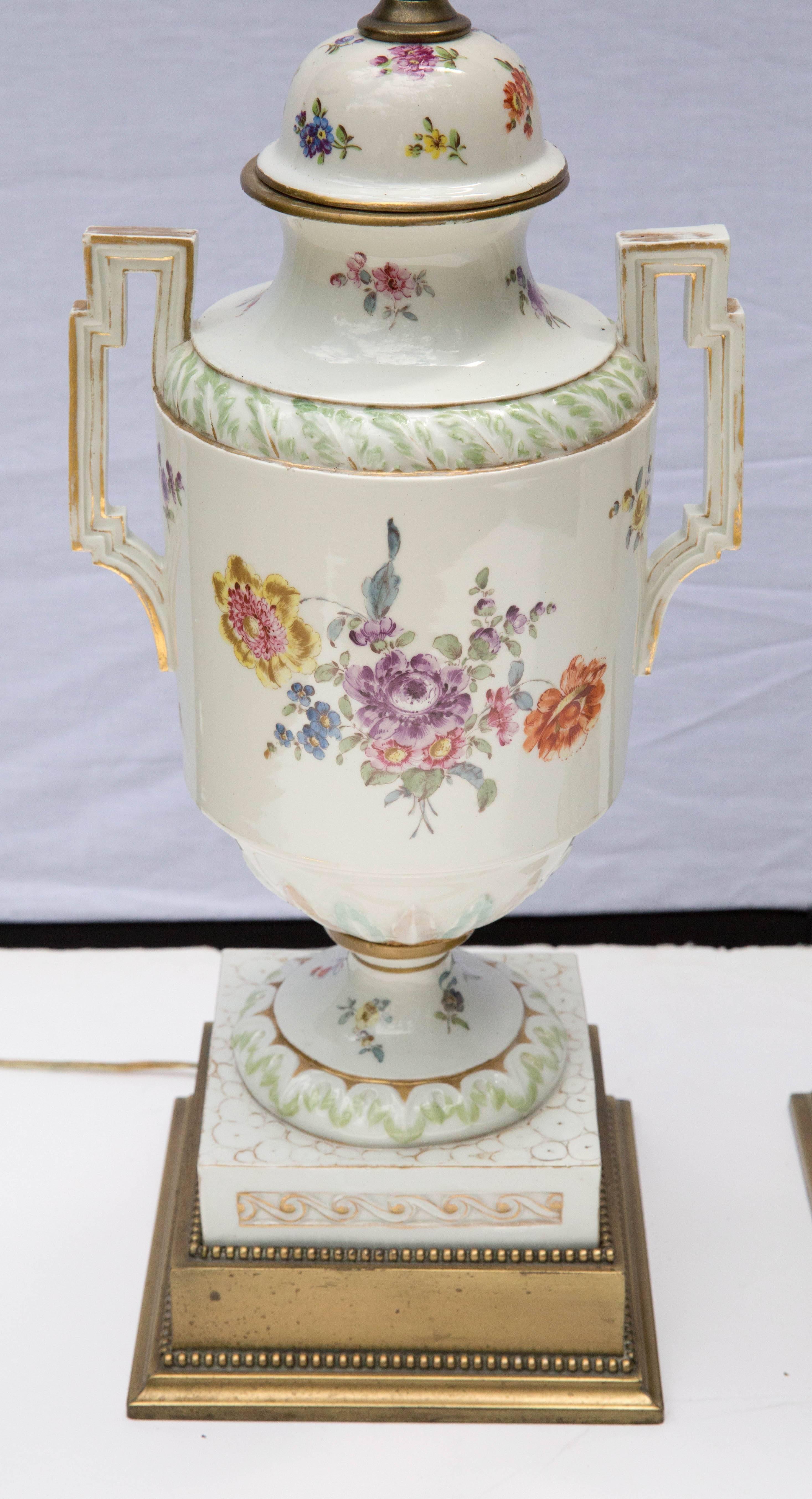 A pair of mid-19th century porcelain dome-lidded urns, hand decorated in the neoclassical manner, drilled and mounted on brass bases, as lamps.