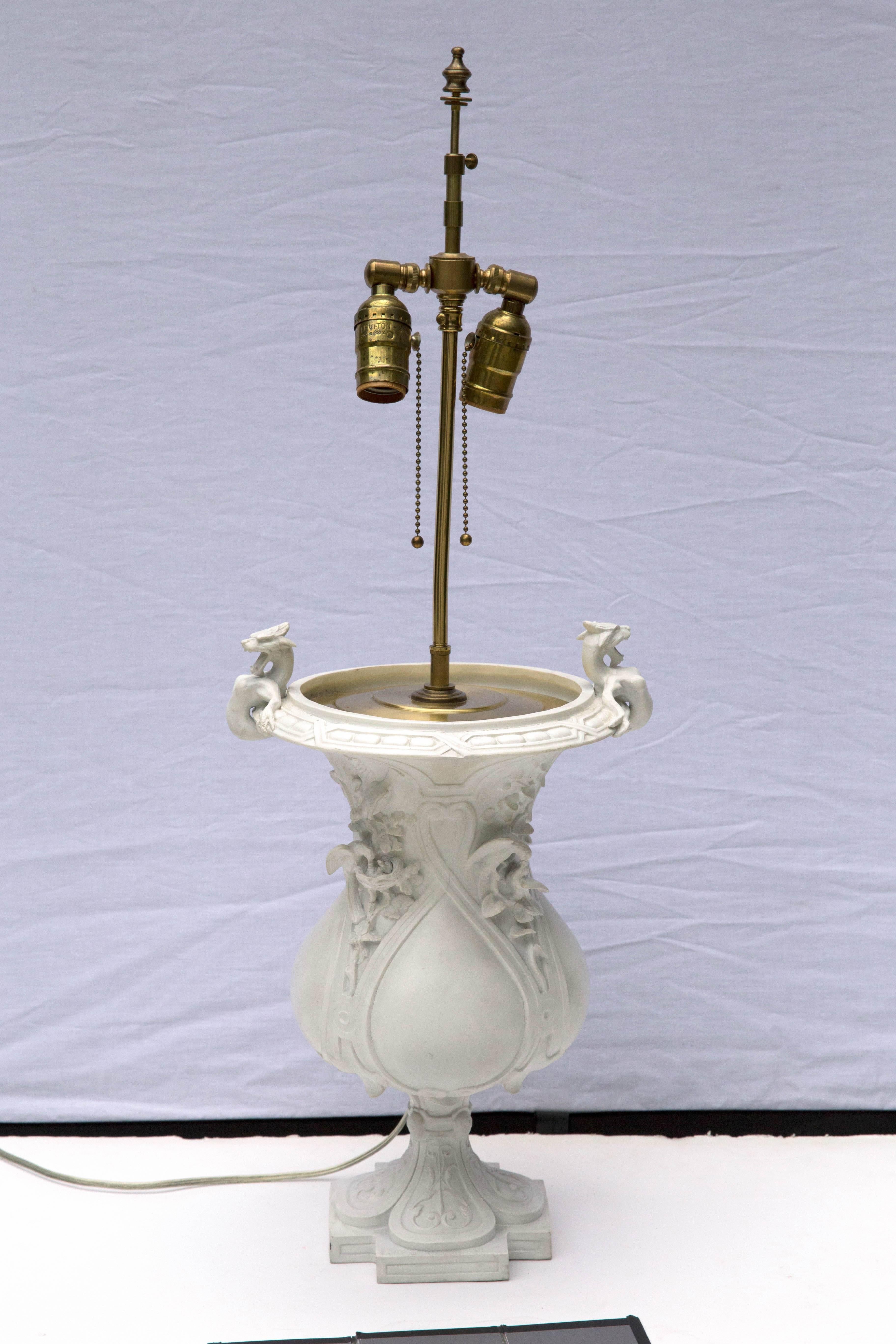A decorative bisque porcelain urn marked by Jean Gille of Paris, France with a raised blue J over G, dating from 1840-1868. Now converted to a two socket table lamp with brass hardware. Measurements are the urn itself.