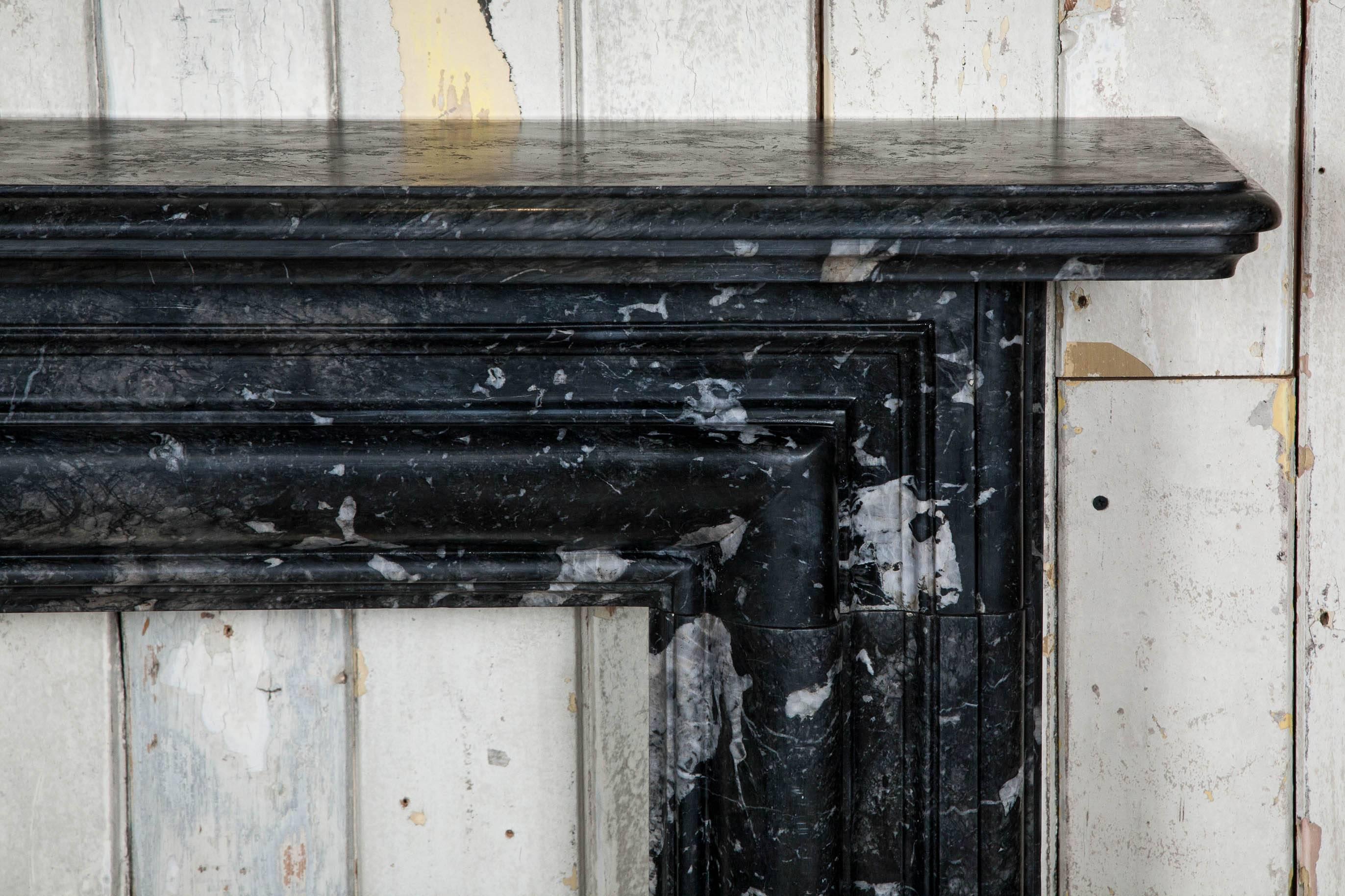 An original late Victorian fireplace surround in highly figured black marble. This antique surround features a moulded bolection surround with a bevelled and moulded shelf. The surround is in distinctive black marble featuring unusual grey