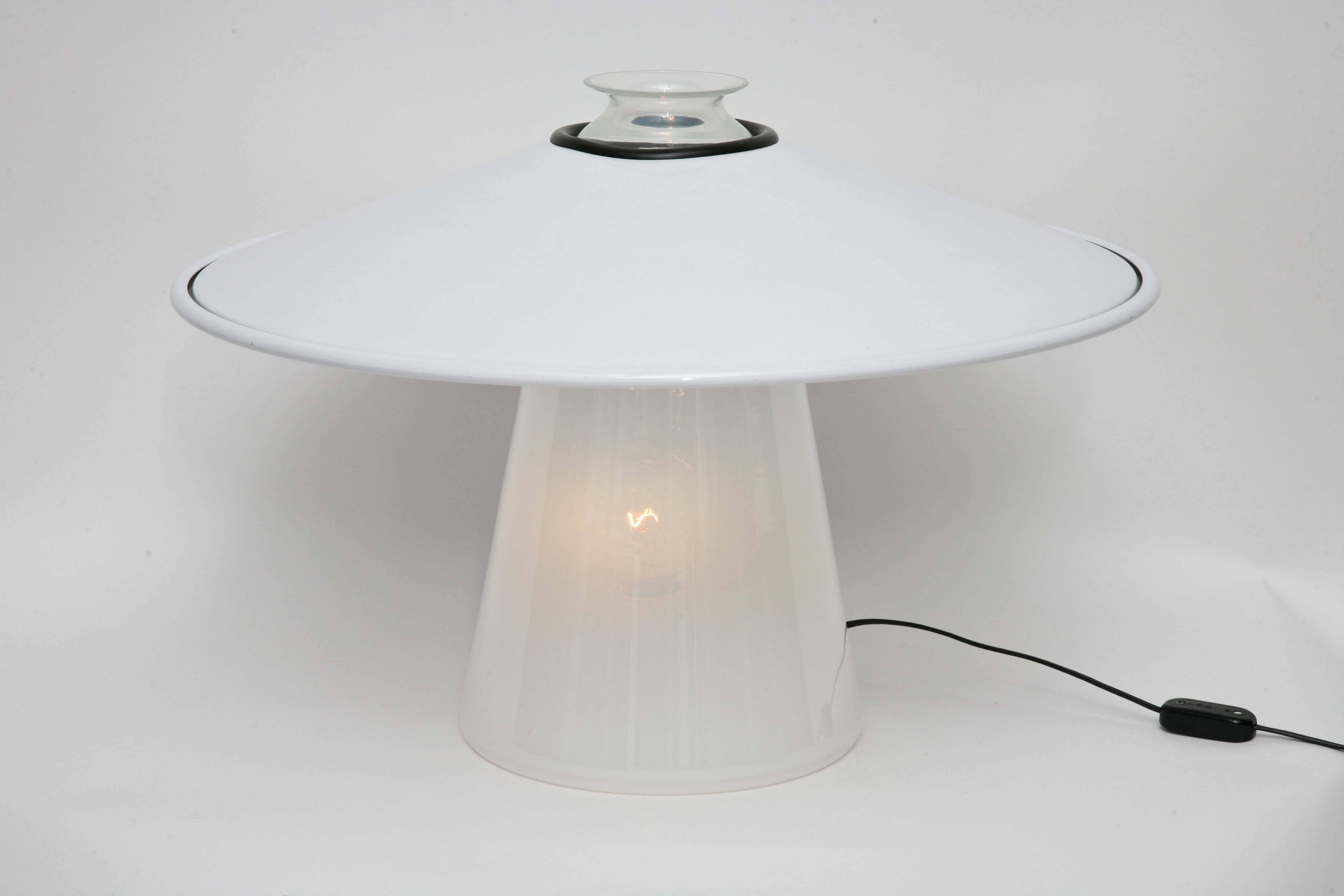 Recalling earlier kerosene lanterns, this 1970s Stilnovo table lamp has a Murano glass body, shading from opaline white at the bottom to nearly clear at the top. The white enameled steel shade has a rubber-ringed opening that fits over the body of