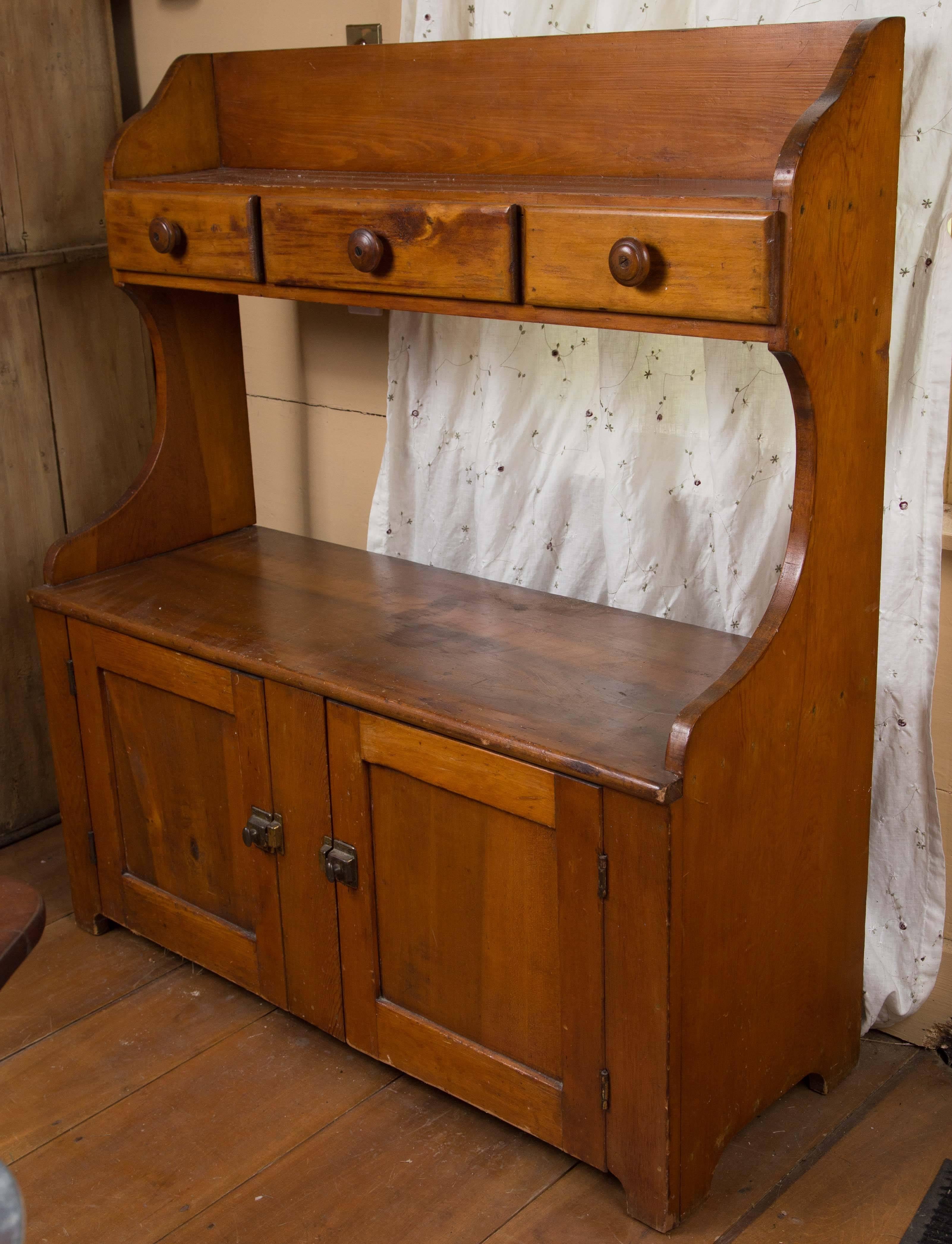 Pine bucket bench with a top shelf featuring three drawers above the bench atop two doors revealing ample storage. Original finish.