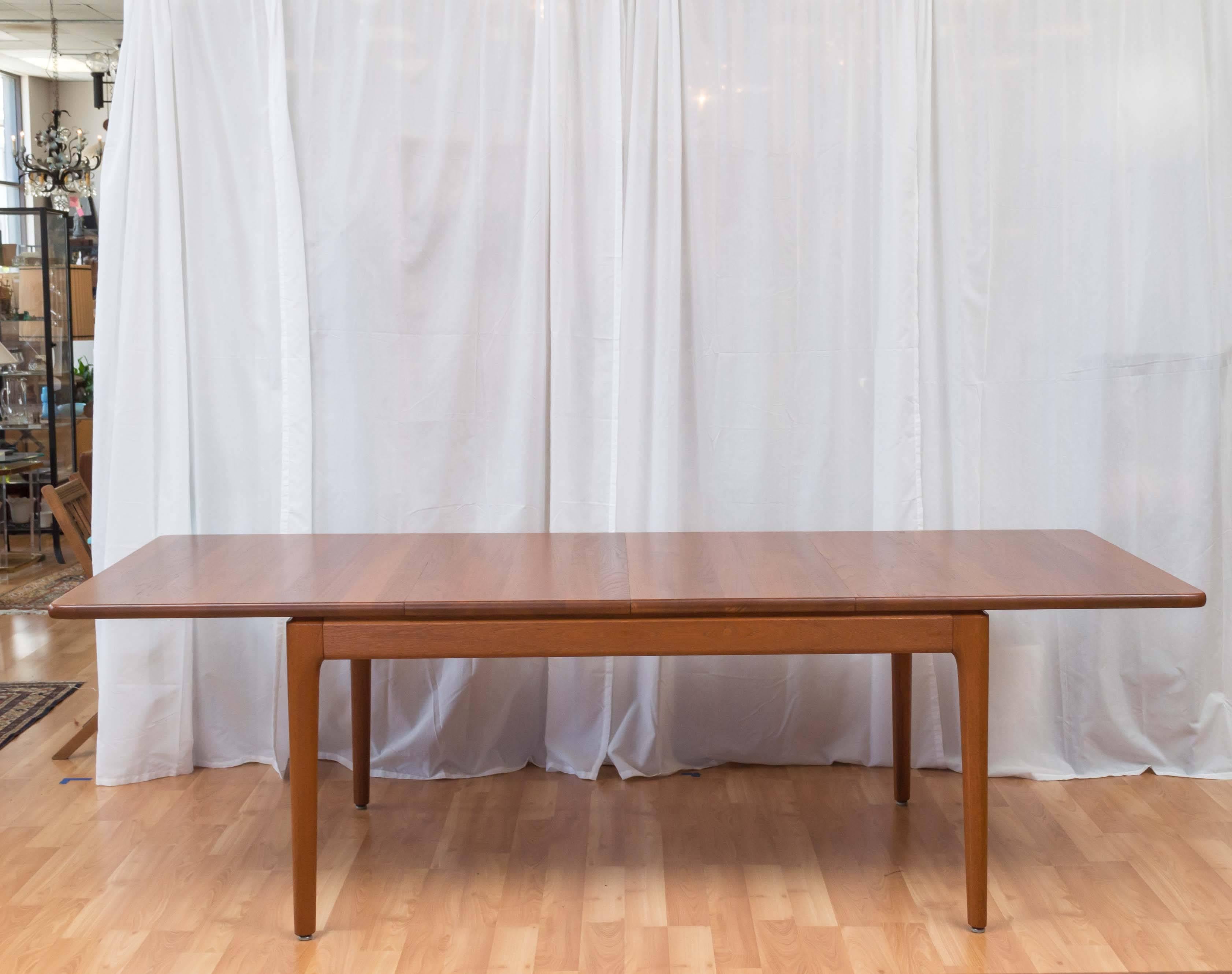 Stunning and large, teak Danish modern dining table, by Glostrup. Table is made of solid teak, which is unusual, most times you'll find the Danish tables to be a veneer. Has two leaves, that you can store under the tabletop when not in use. A