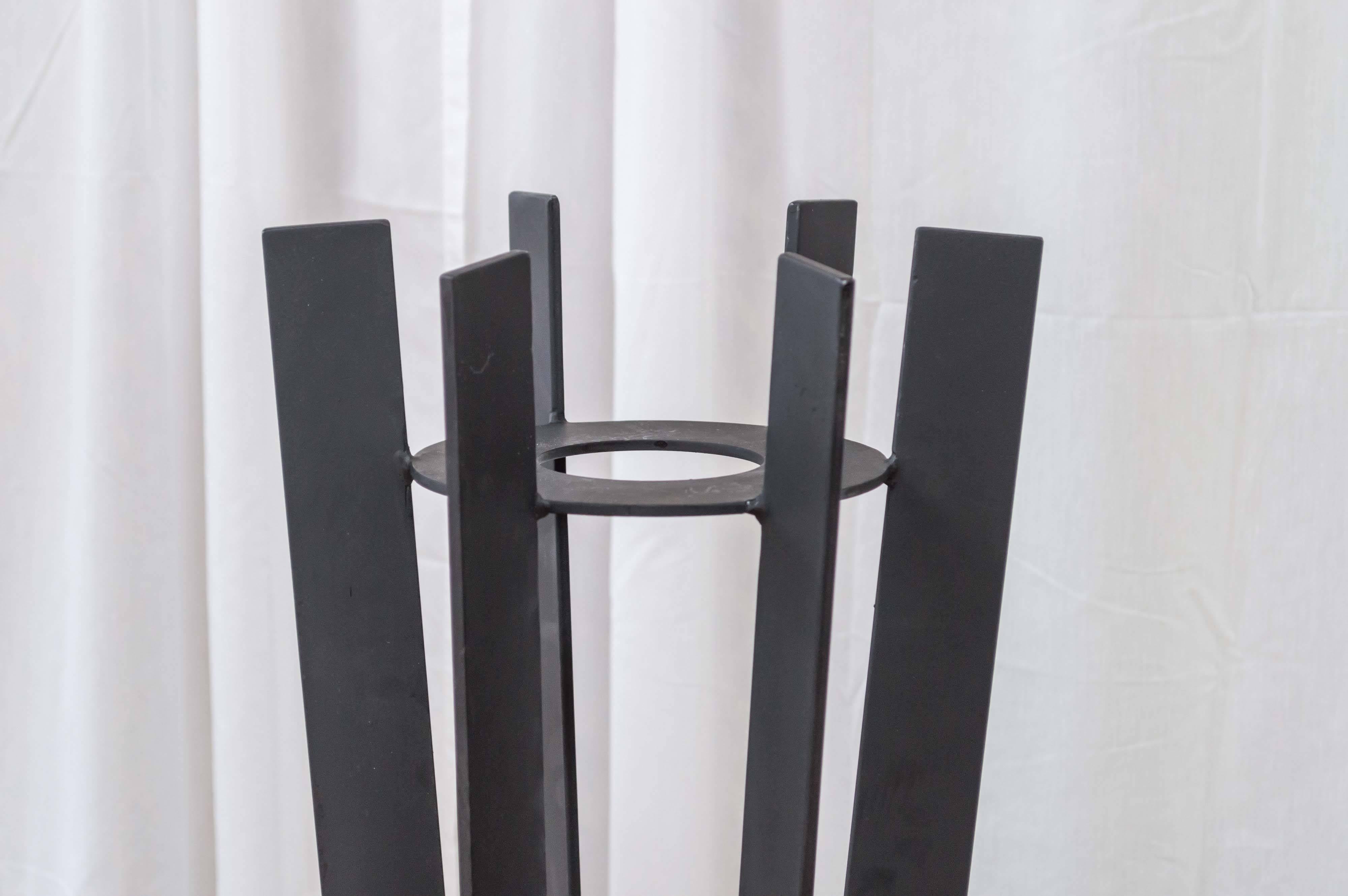 A pair of tall wrought iron plant stands that are as sculptural as they are functional.

The body and base are each comprised of six 2 in deep, matte black fins. They support a 7.50 in circular shelf with a 3.50 in opening in its center, on or in