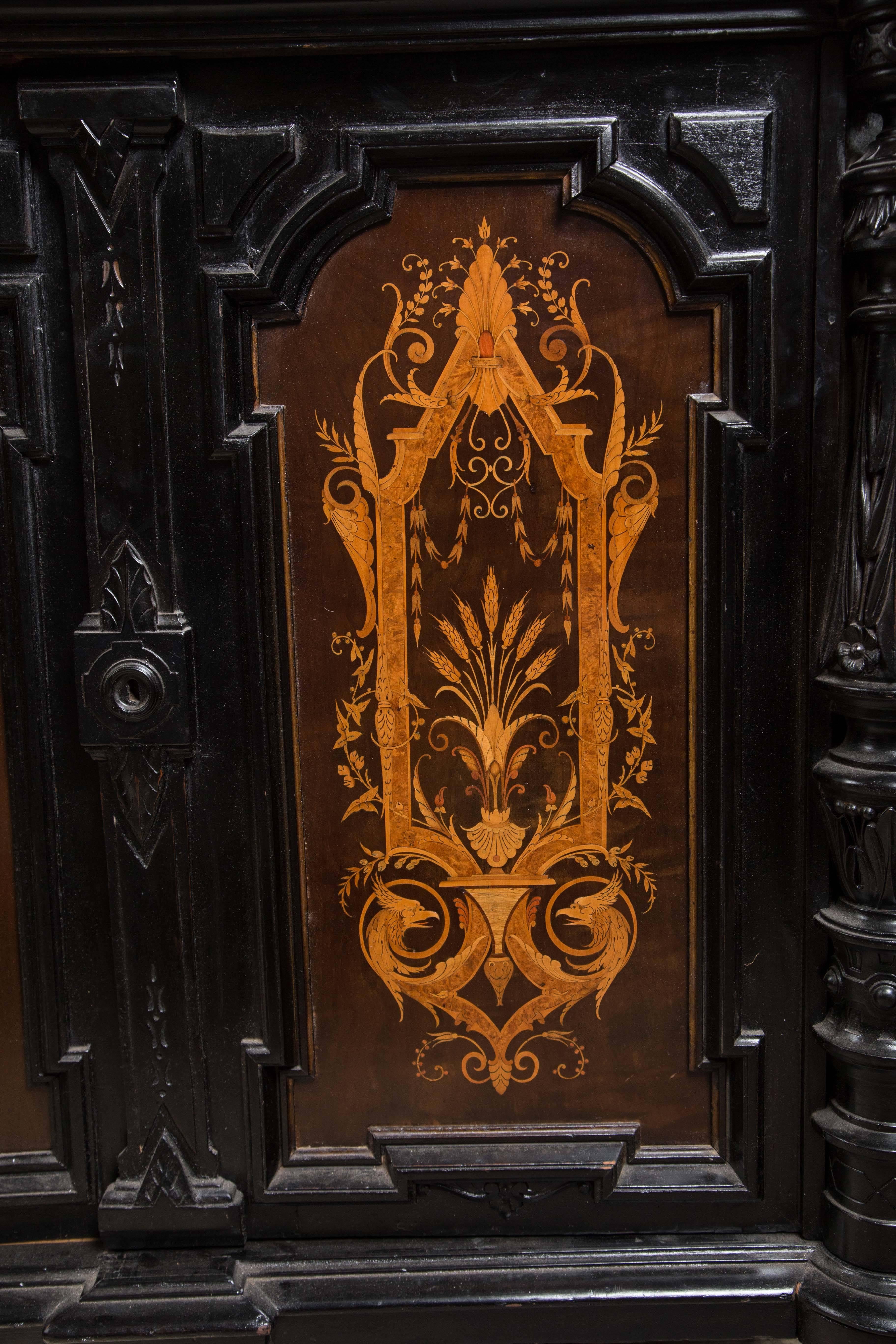 The top is solid black with turret corners in front. Separate turned and carved columns flank the two doors. They are inlaid with panels of satinwood and other woods with classical motifs, as are the side panels. Raised on turned short feet. Inside