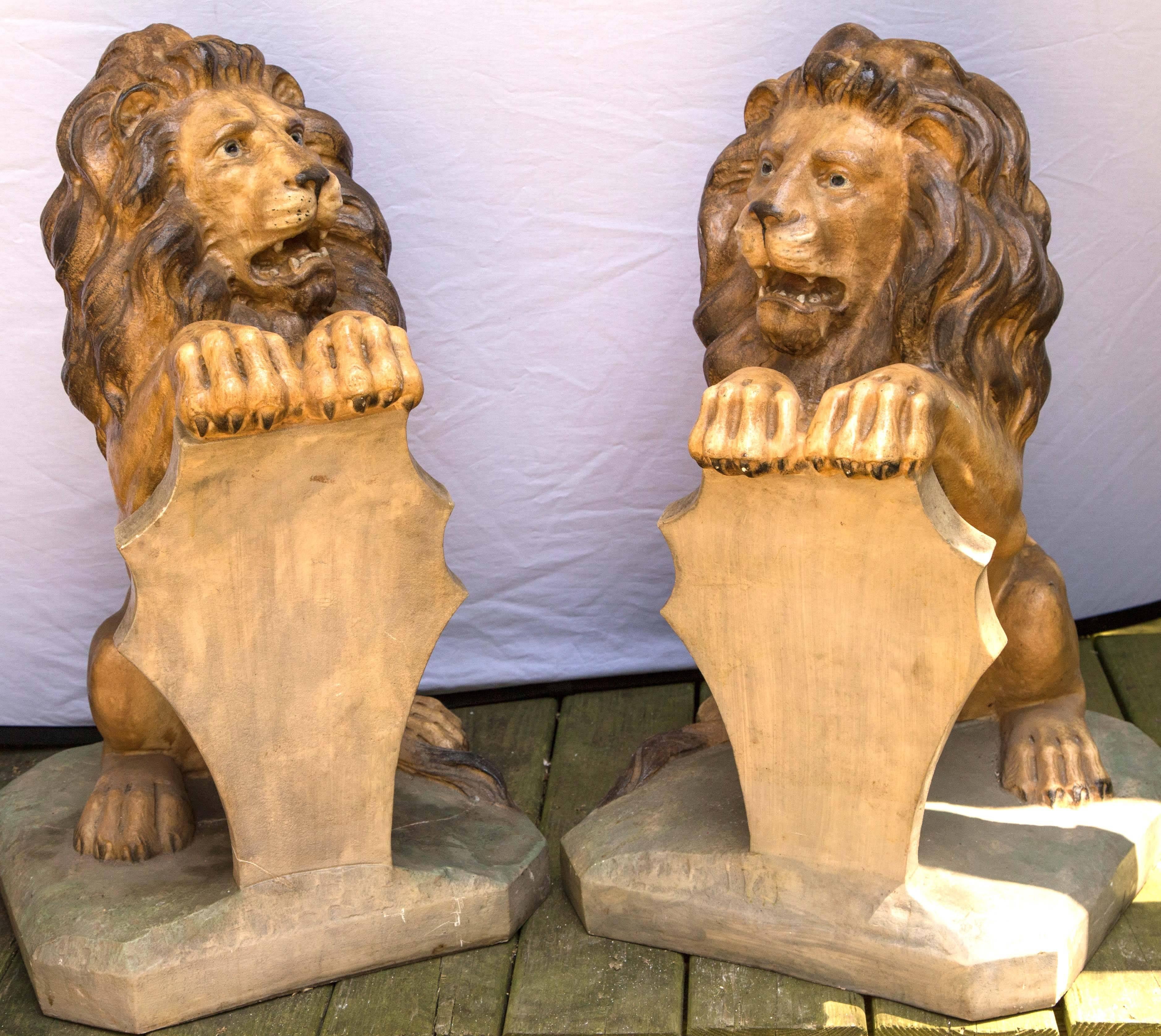 These lions of cast stone have been painted in realistic colors. They sit on their haunches while holding a shaped shield.
 The bases have cut corners. One toe on a rear foot is chipped, there is a hairline crack in one base and there are small