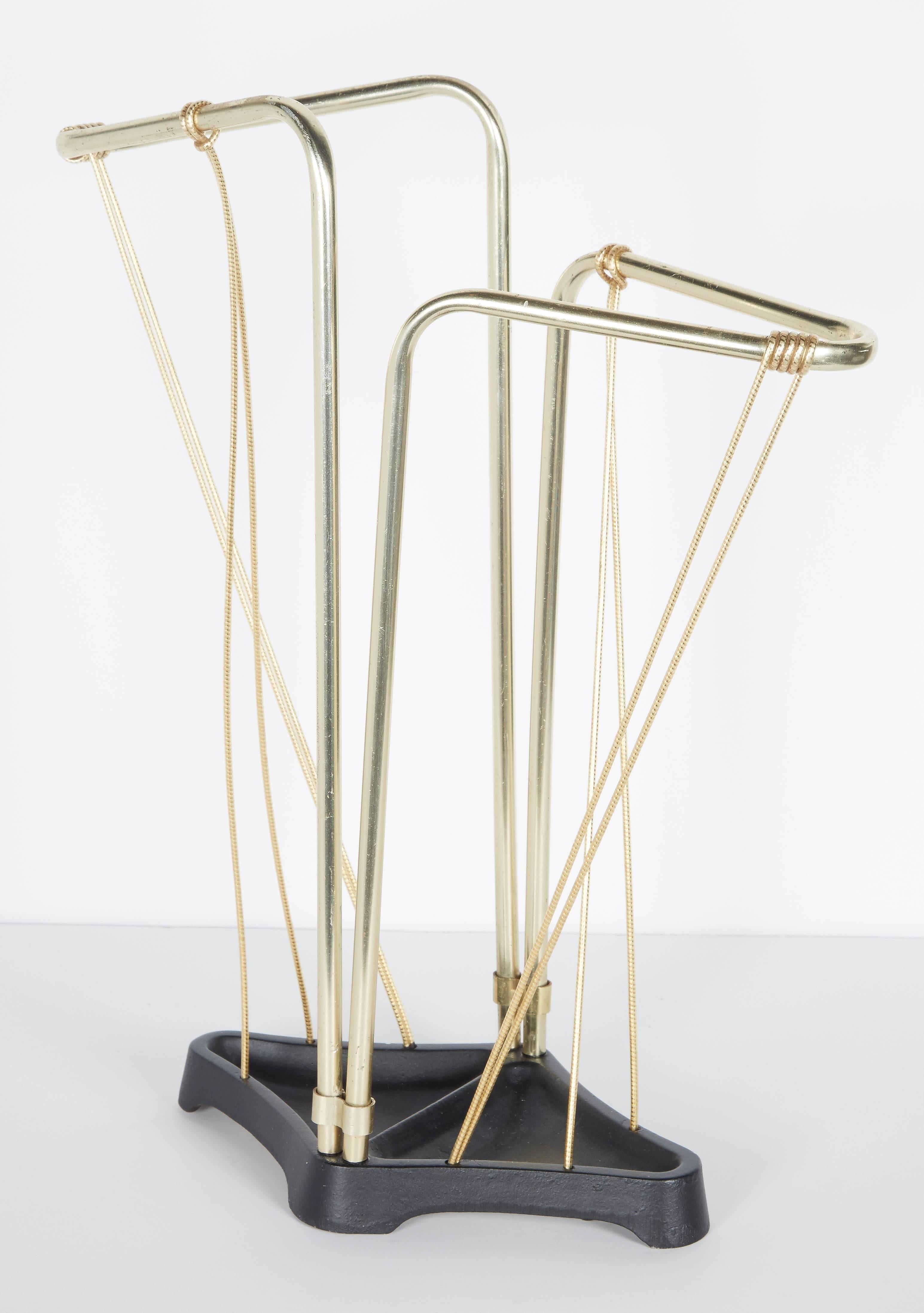 Outstanding Mid-Century umbrella stand with ultra modernist design. The stand features a winged form with asymmetrical design. Comprised of brass tubular metal with a black enameled wrought iron diamond shaped base. The umbrella stand also features