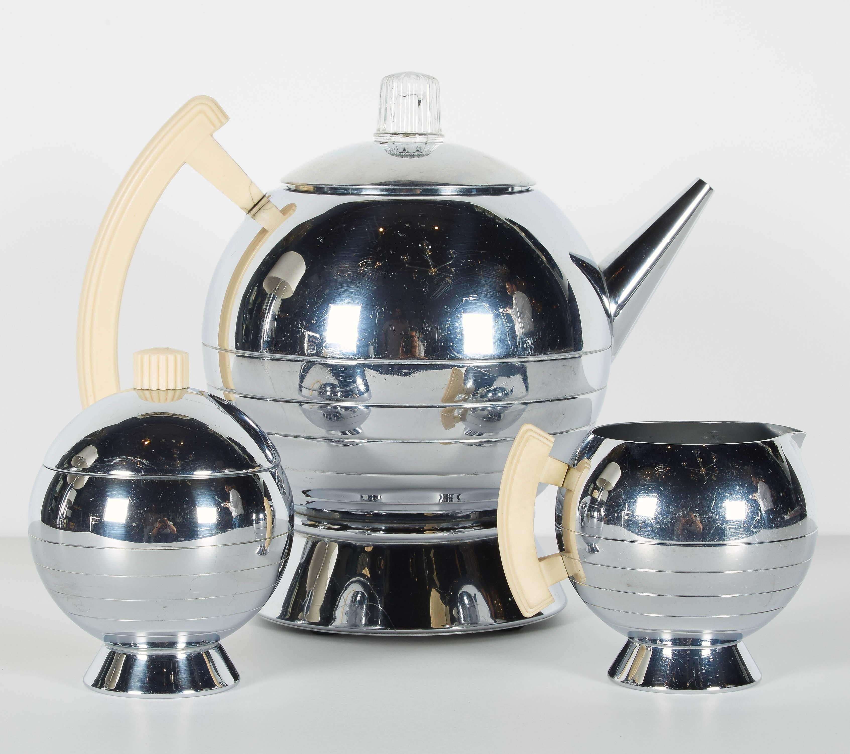 Iconic Art Deco coffee and tea service set with stylized Machine Age design. All pieces have chrome finish with bakelite handles and accents in ivory and cognac. The serving set includes an electric coffee pot, sugar, creamer, serving tray, and