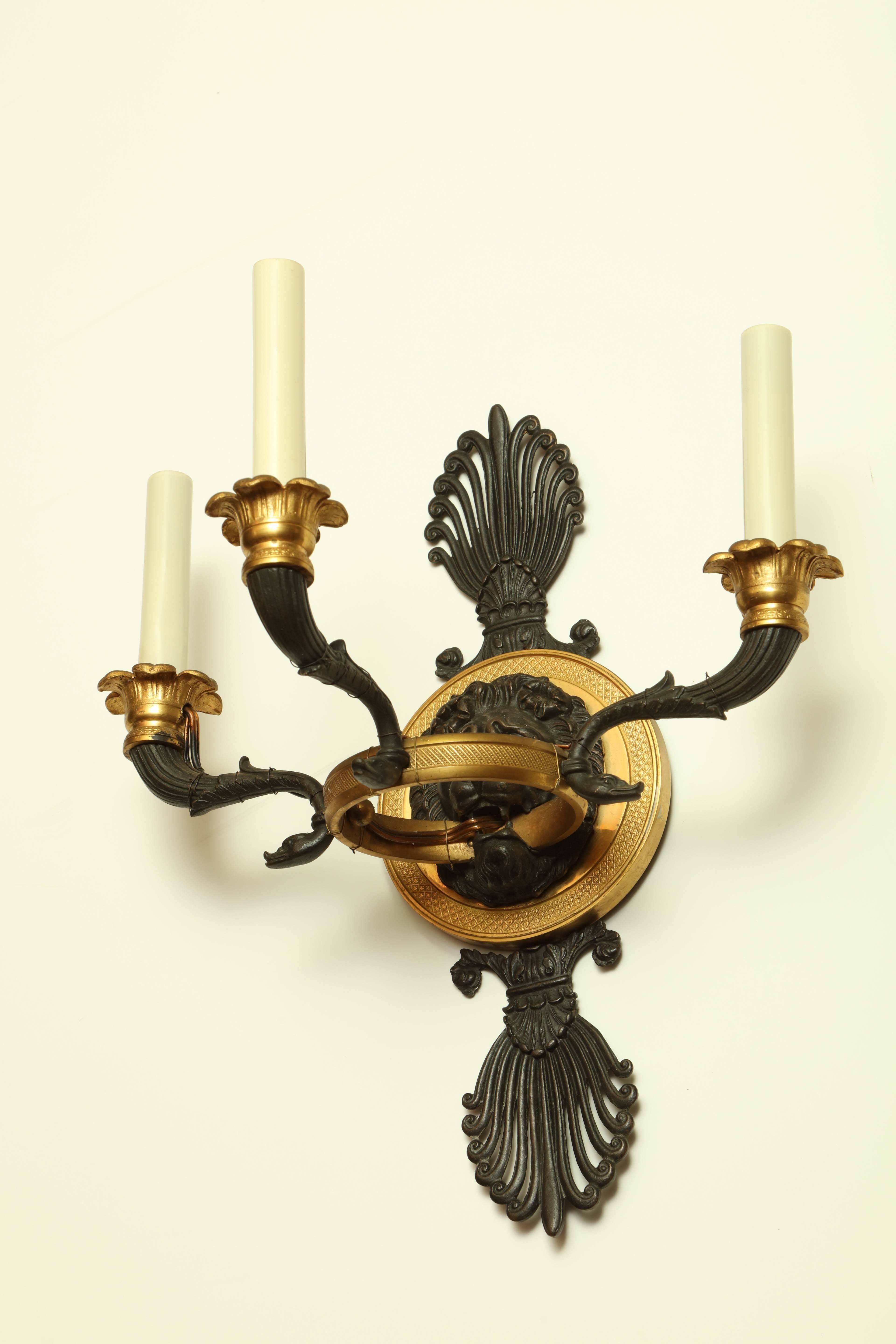 Pair of French Empire gilt bronze and patinated lion head three-light sconces.