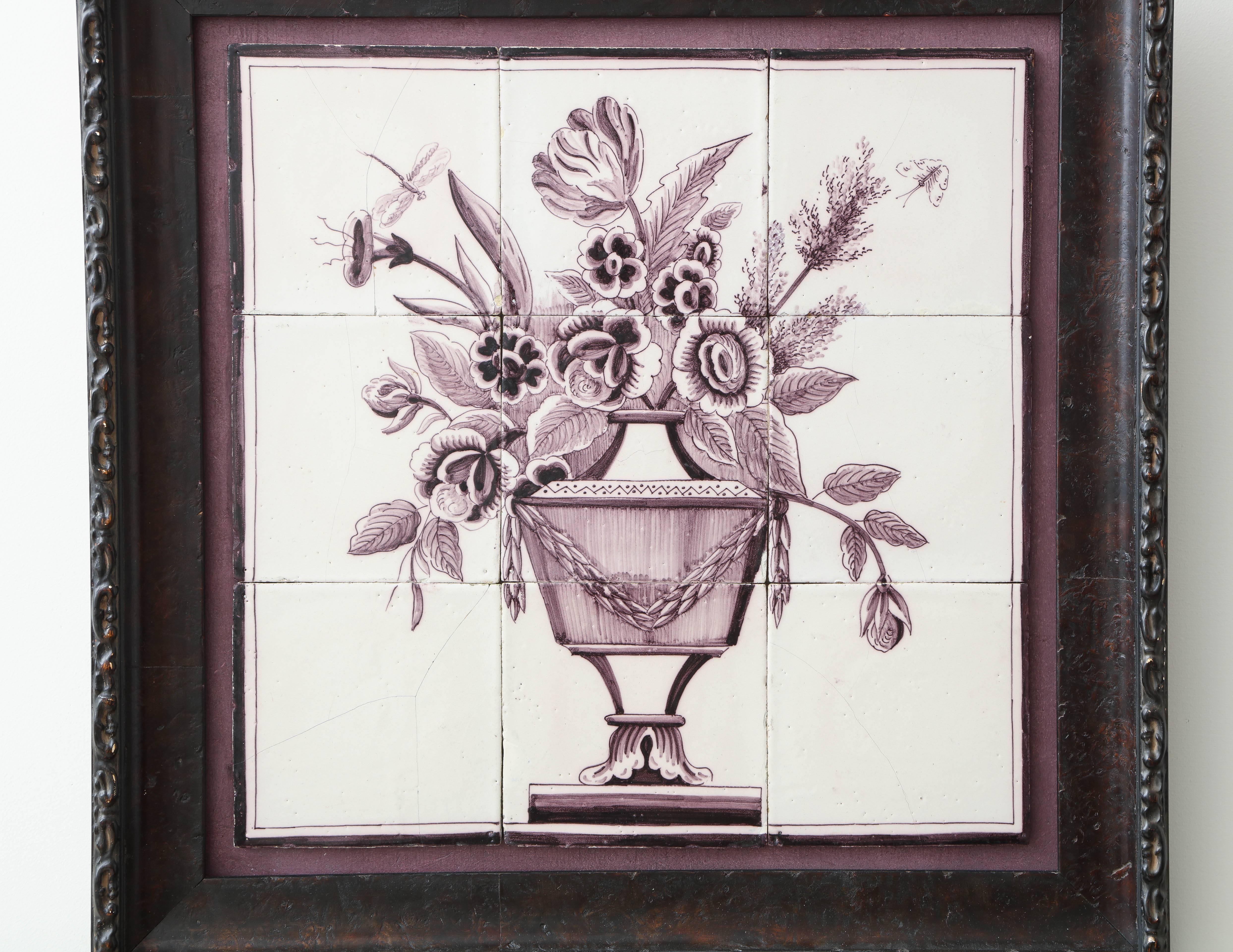 A late 18th century Dutch delft manganese tile picture of a neoclassical urn with flowers and insects in a later carved wood frame.