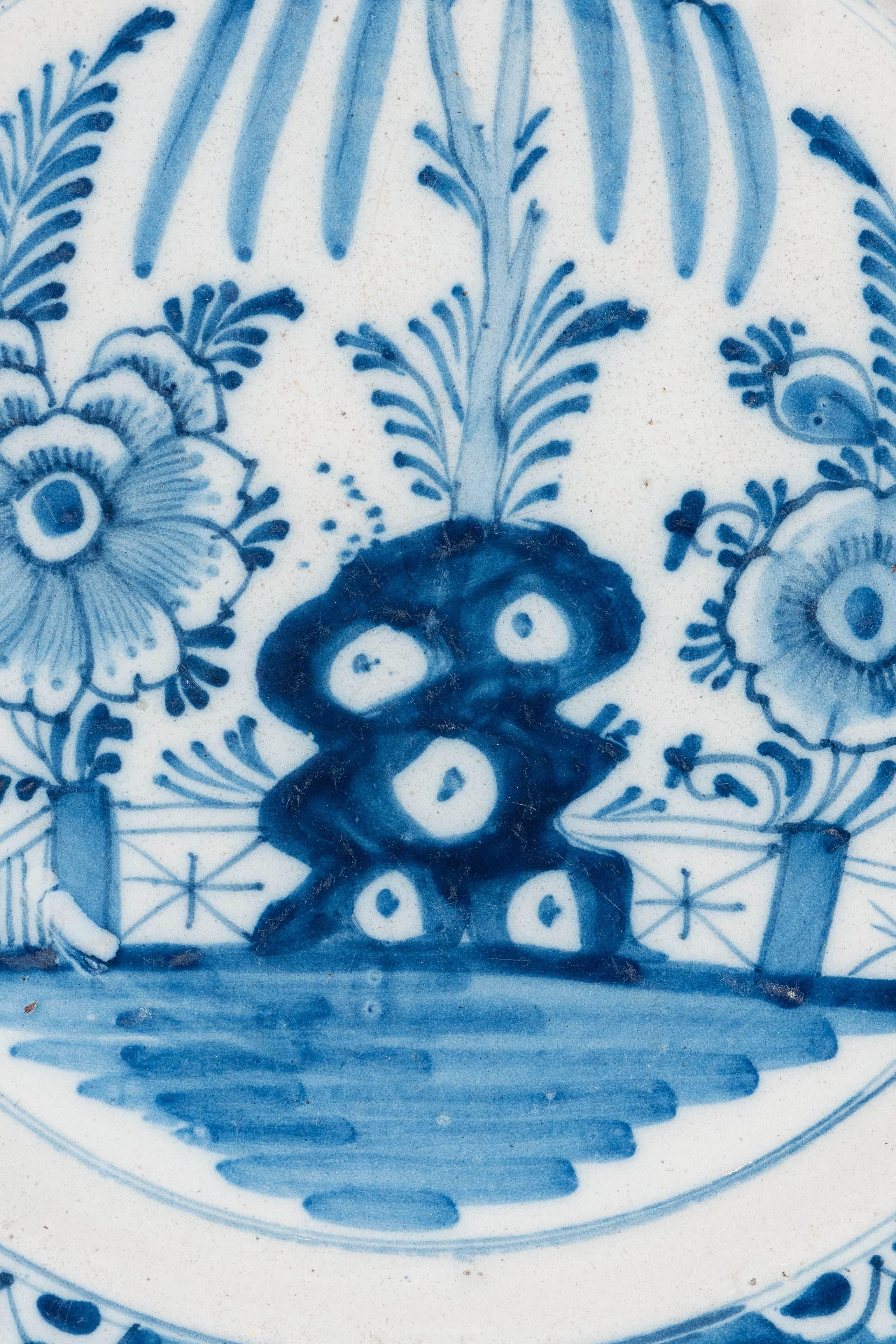 We are pleased to offer this pair of Blue and White Delft chargers hand=painted with a naive garden scene. The oversize flowers and the taihu rock are seen in front of the garden fence. The cobalt blue border is decorated with flower heads painted
