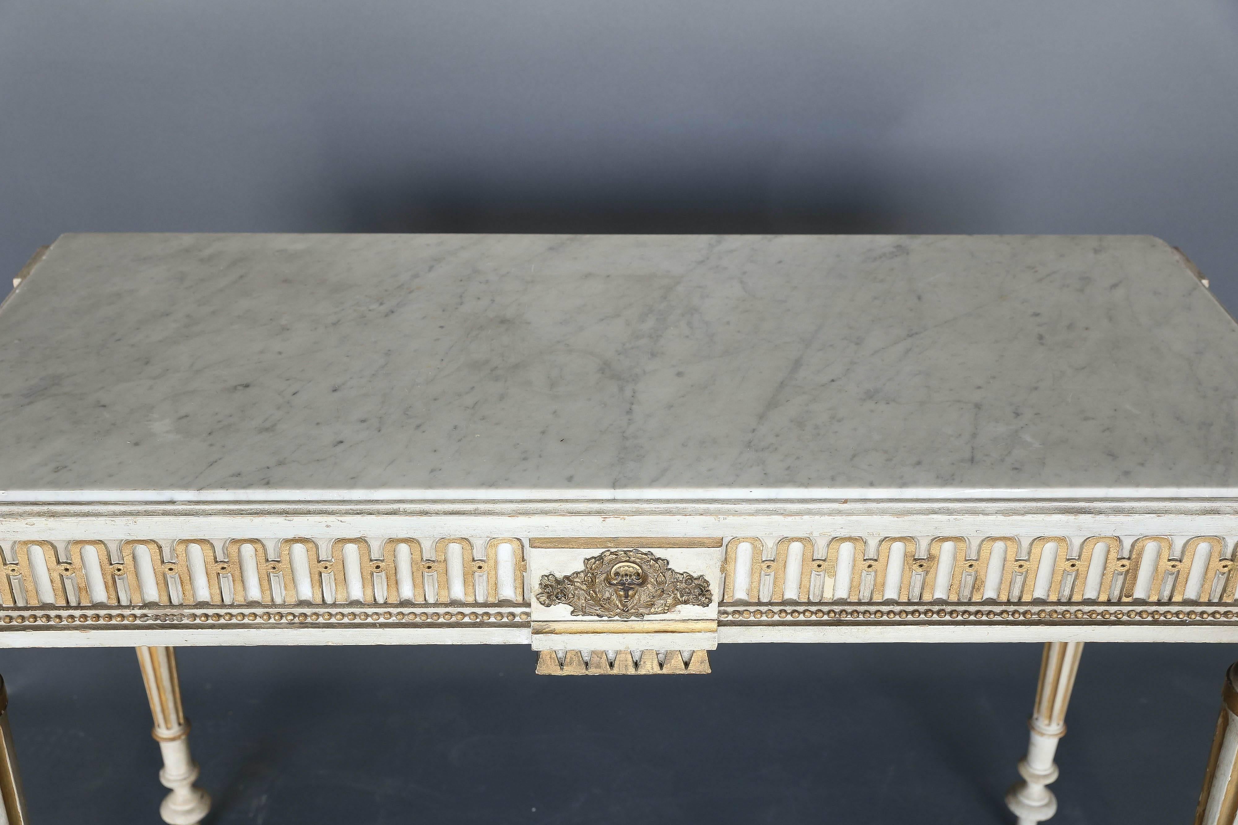 Narrow French console with medallions in corners, gallery detail along the skirt and well-proportioned carved legs. Gold and white paint design with an original soft Carrara marble top.