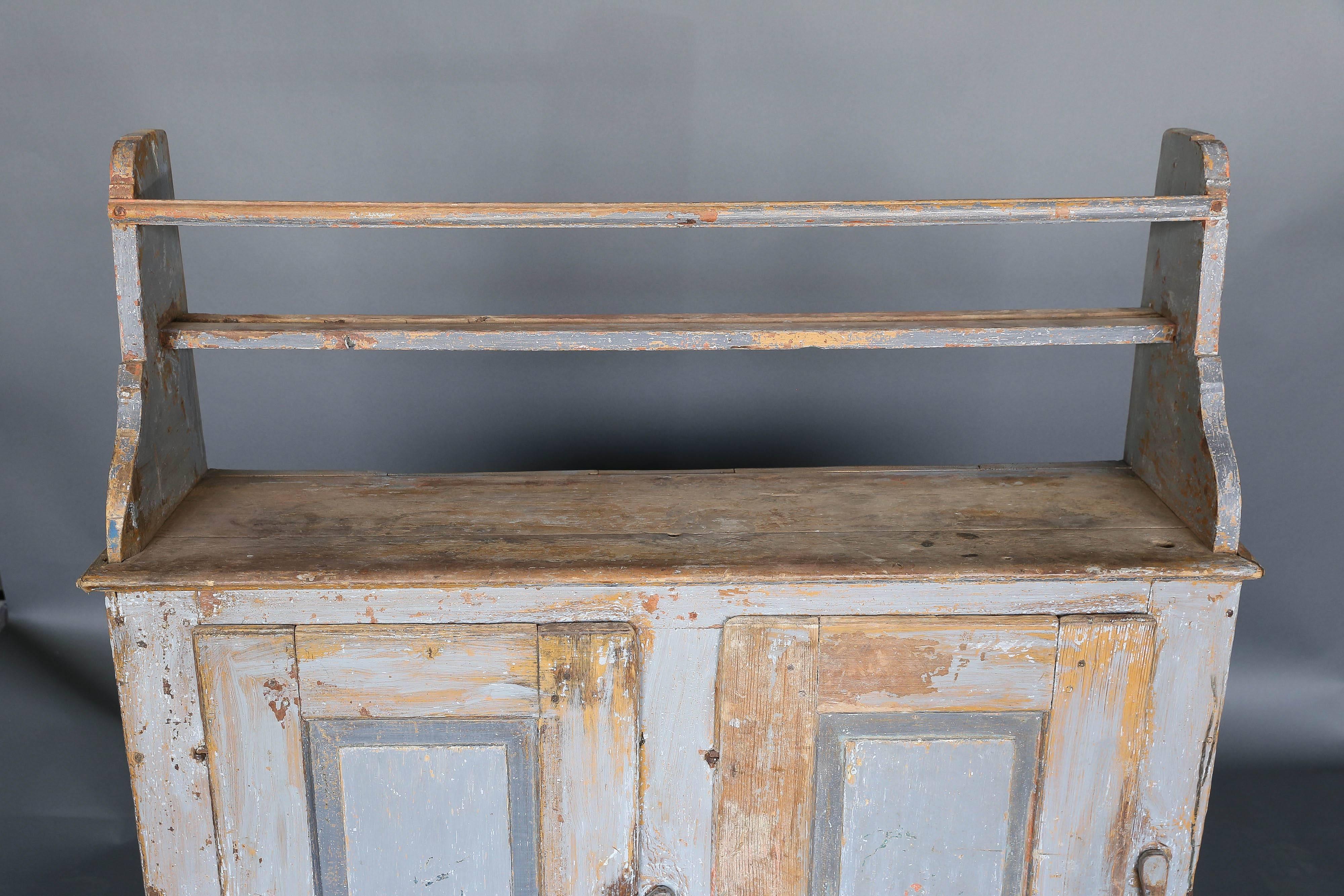Antique primitive 18th century narrow Swedish cabinet with shelf in a beautifully worn light blue paint. Clasps on pair of cabinet doors are wood. Sculpted shelf with rack. Charming country piece.