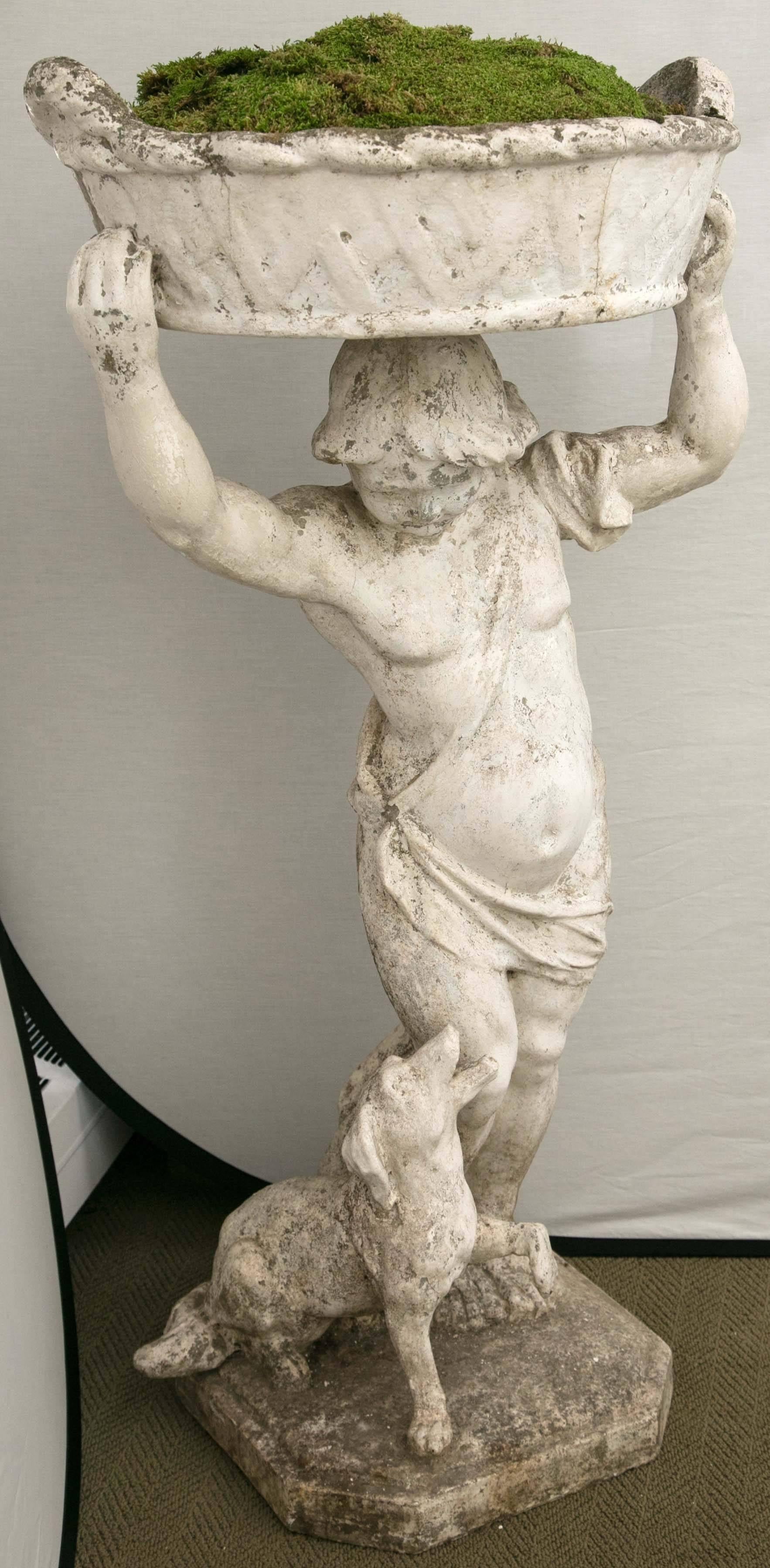 Statue of a boy holding a planter basket on his head with a little dog at his feet.