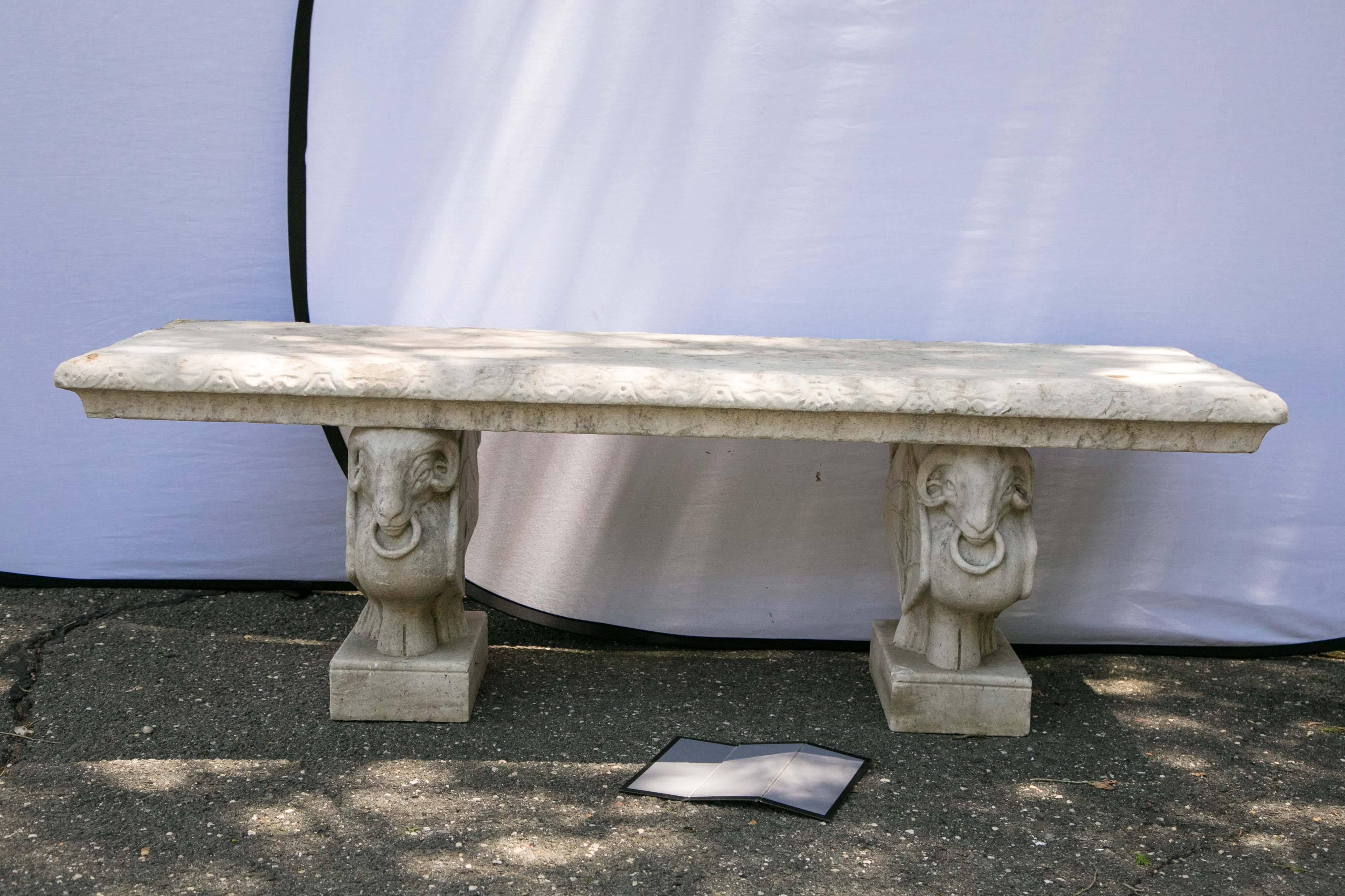 Carved marble garden bench having a thick top supported on winged ram carved bases with ring decoration.