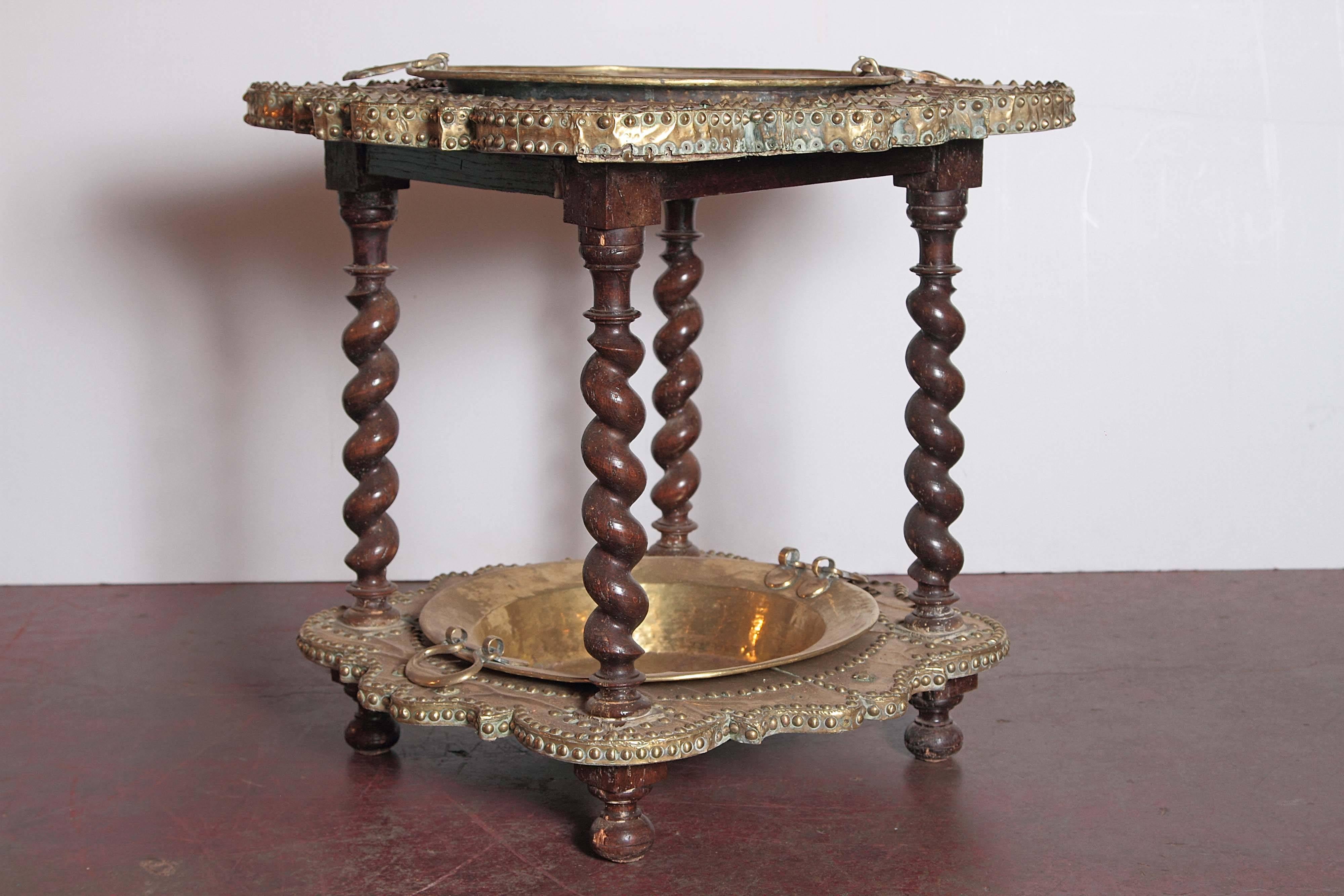 This unique, interesting fruit wood brasero was crafted in Spain, circa 1780. The antique table features four walnut barley twist legs, and two removable brass trays. The rustic piece is embellished with geometric motifs and designs, and is complete