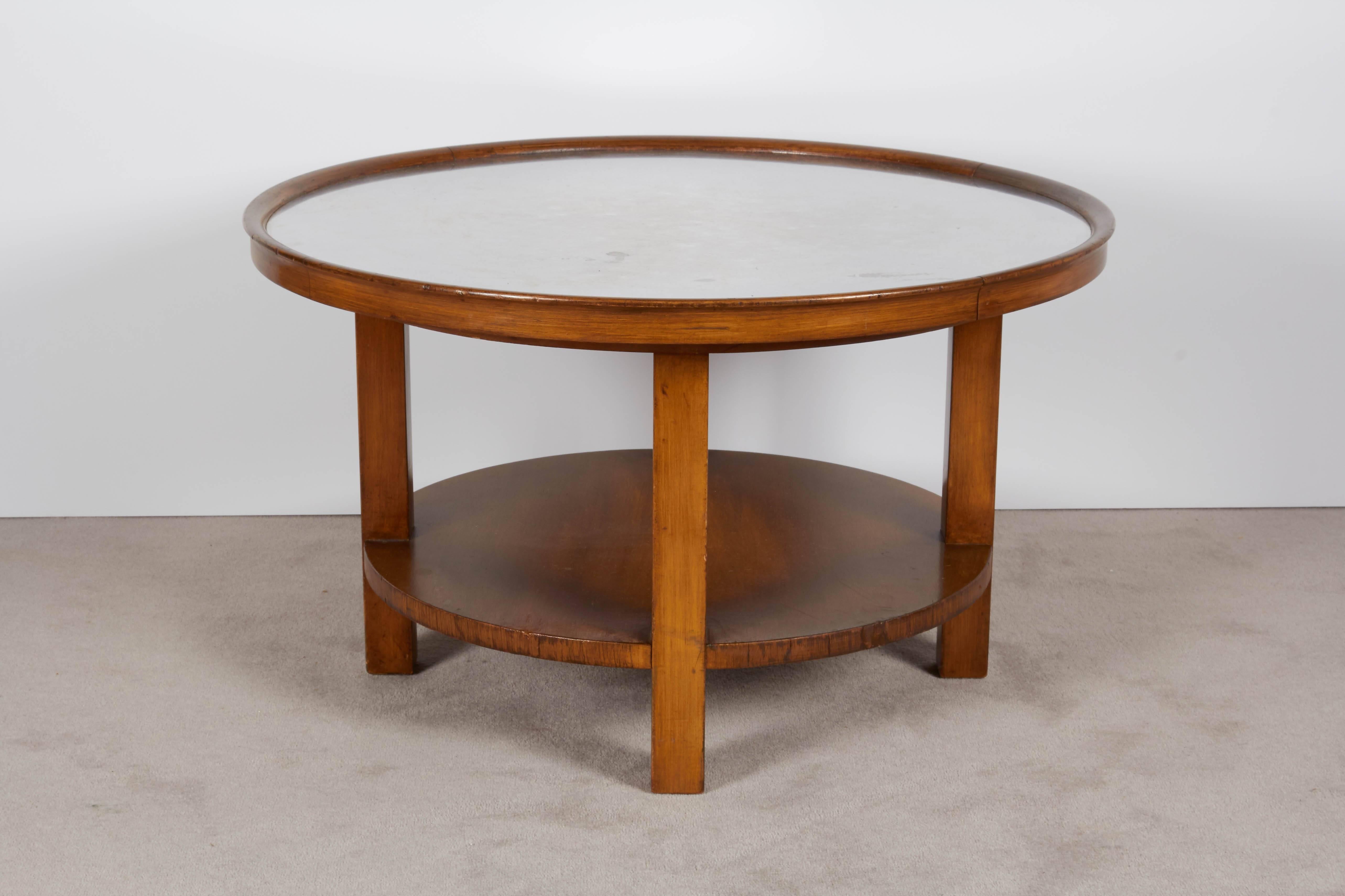 A round coffee and cocktail table, produced by Johnson Furniture Co. for John Stuart, circa 1950s, with aluminum top, set against a wood frame with lower tier. Markings include stamp [FHA/Johnson Furniture Co/Grand Rapids Mich.] and plaque [John