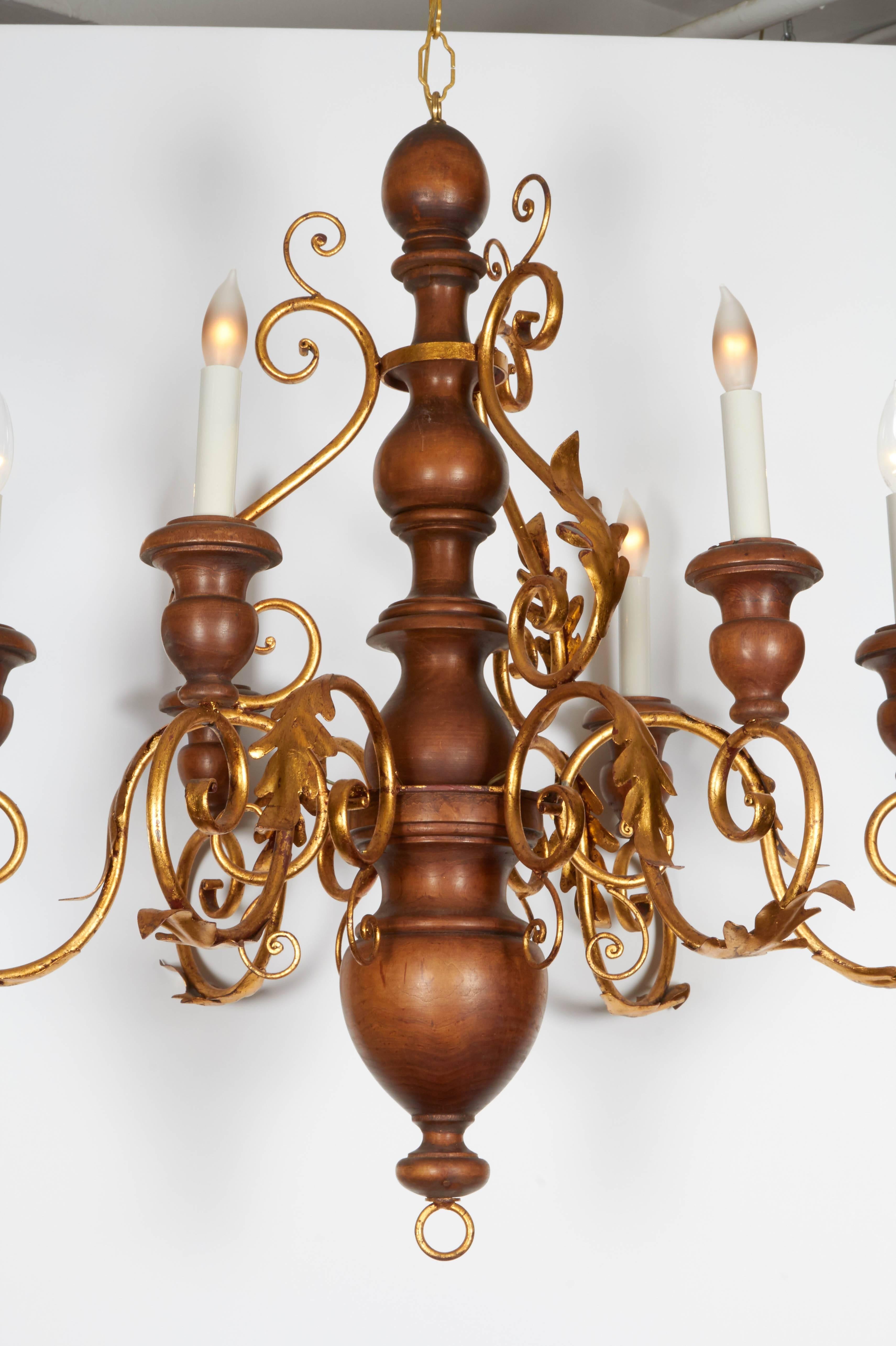 A Florentine six light chandelier, produced, circa 1950s, with turned, baluster form wood body and decorative bobeches, each with faux candle socket cover, and scrolling arms, accented with oak leaves, in gilded metal. Wiring and sockets to US