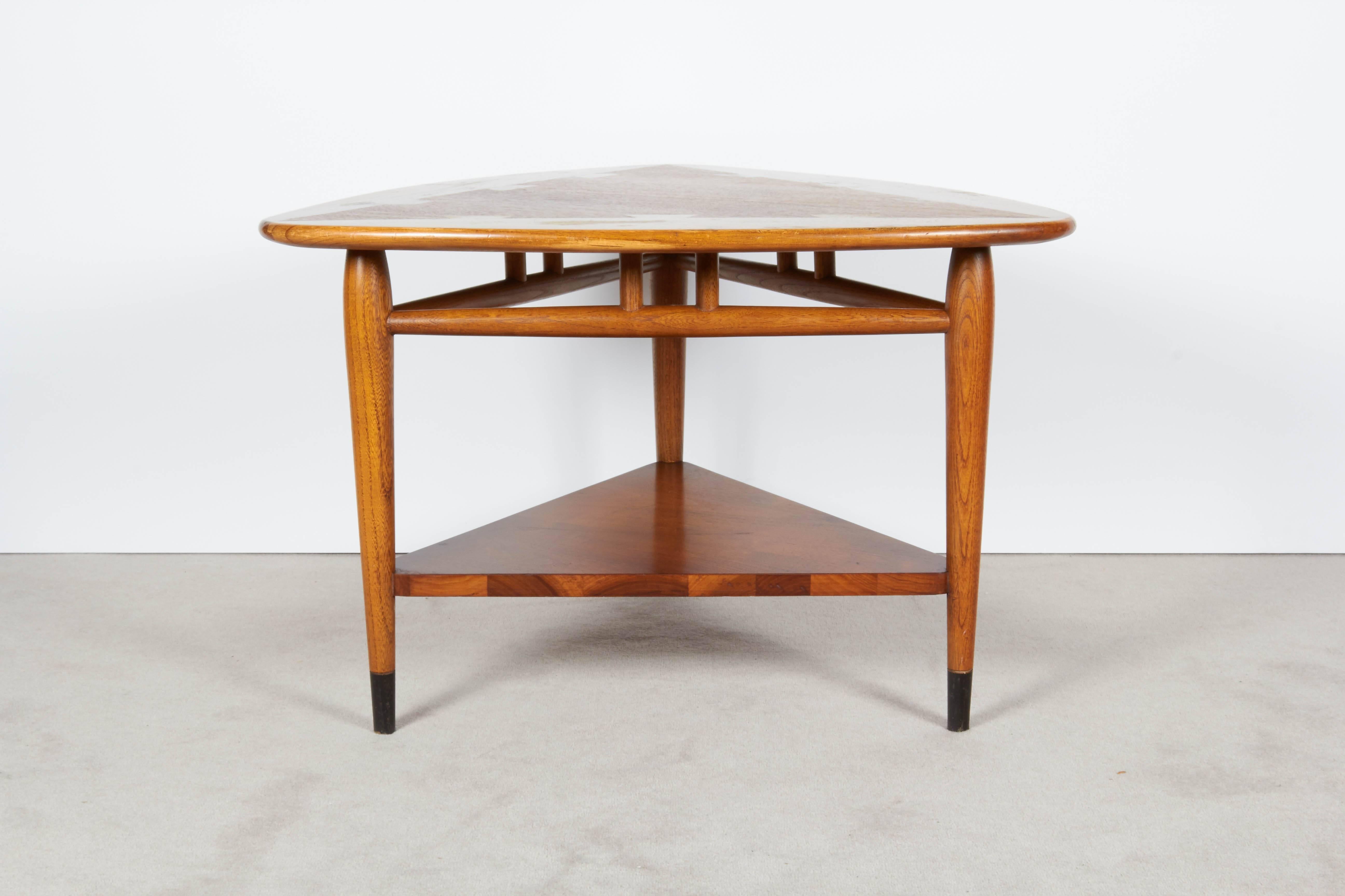 A triangular walnut table, produced by Lane, circa 1950s-1960s, with dovetail details to the top perimeter, on three tapered legs, and over a lower tier. Markings include manufacturer's stamp [Lane / Altavista, Virginia] and the serial number